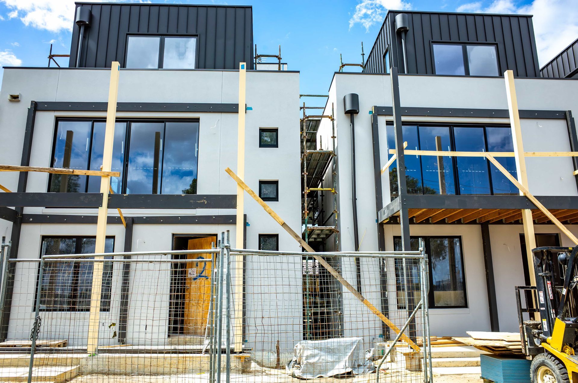 Two houses are being built next to each other on a sunny day.