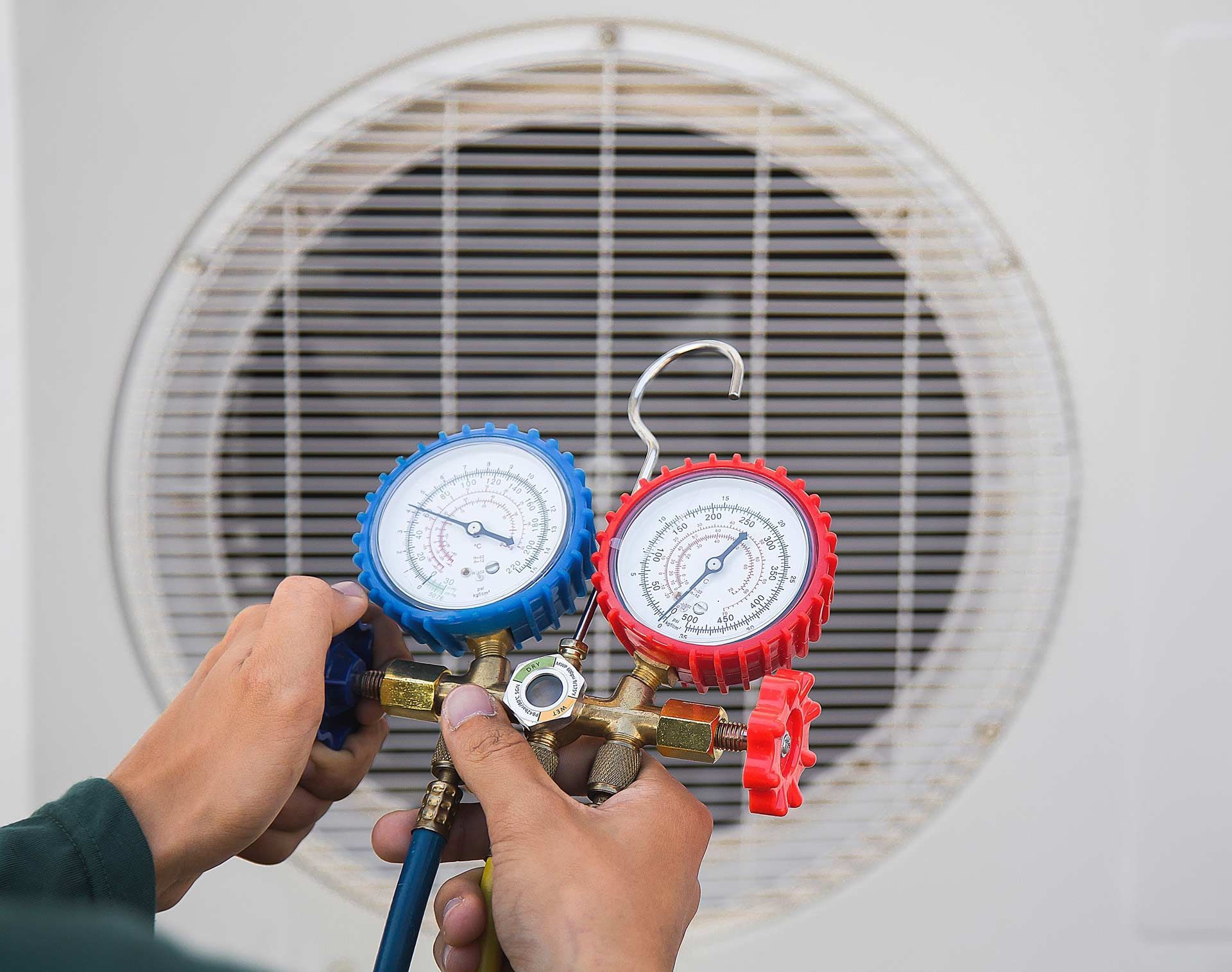 A technician using gauges to check an air conditioning unit outdoors.