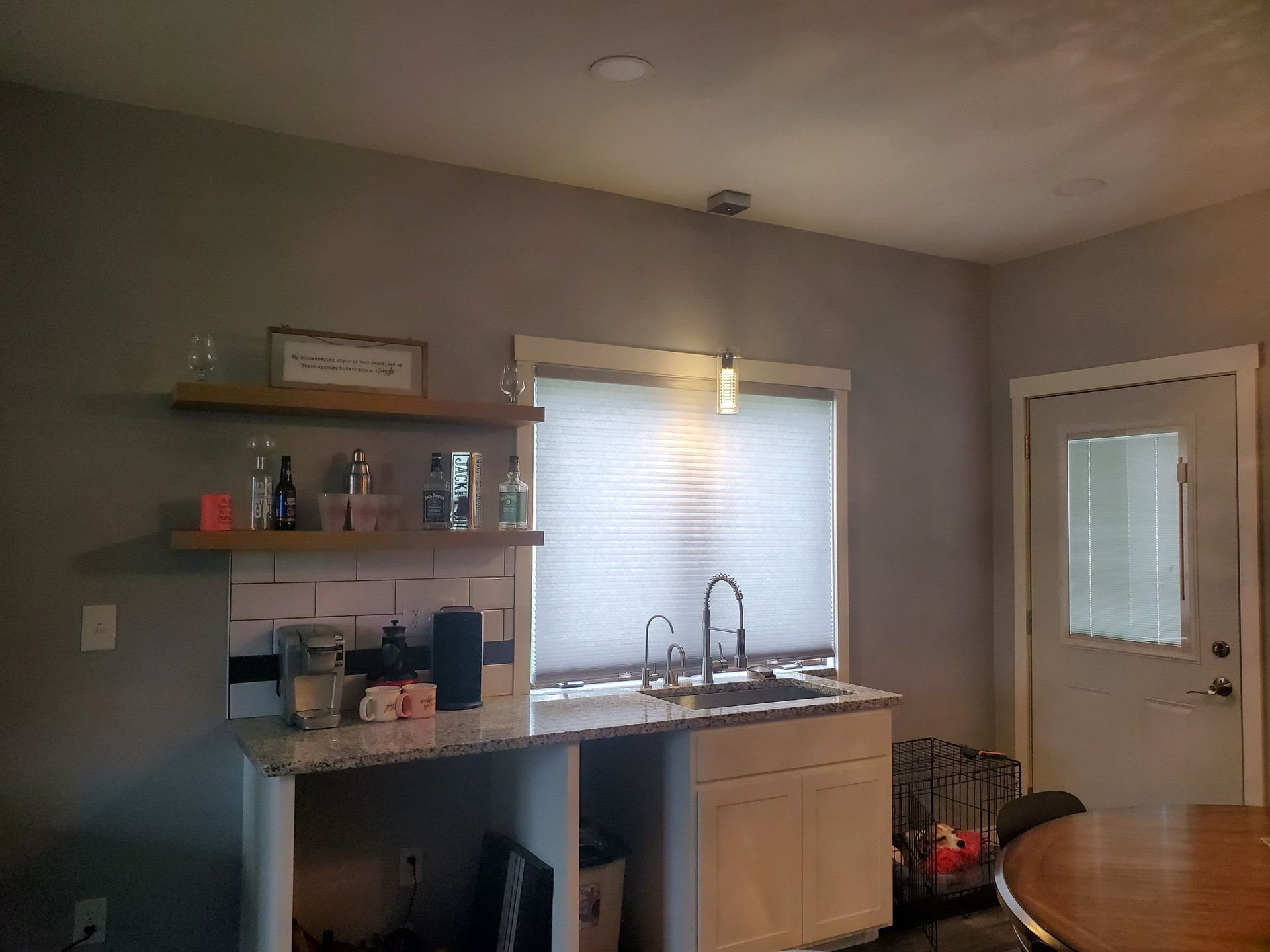 Kitchen area with sink, cabinets, shelves, and a door. Gray walls, white cabinets, and neutral decor.