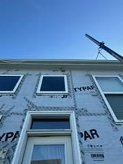 Exterior of a house with windows covered in Typar material; crane in background against blue sky.