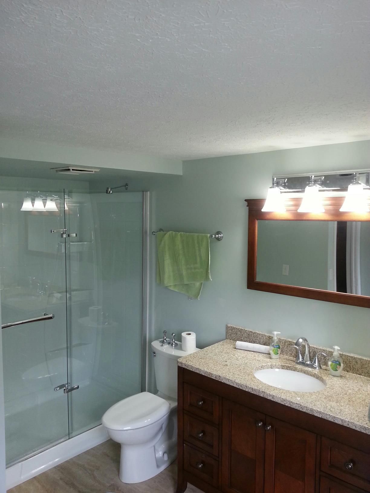 Bathroom with shower, toilet, vanity, and mirror. Light blue walls, brown vanity with granite countertop.