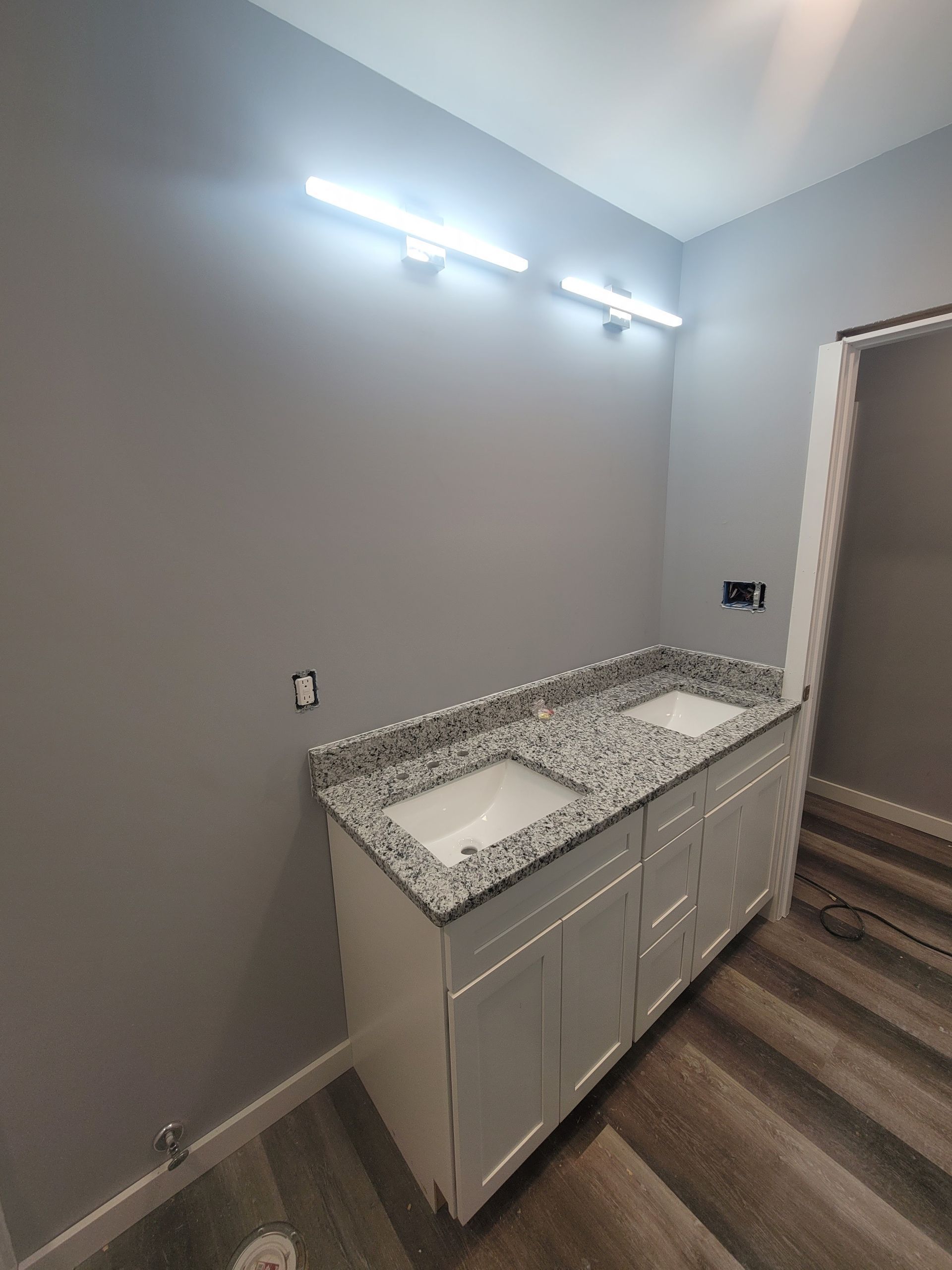 Bathroom with gray walls, white double vanity, granite countertop, and wood-look flooring.