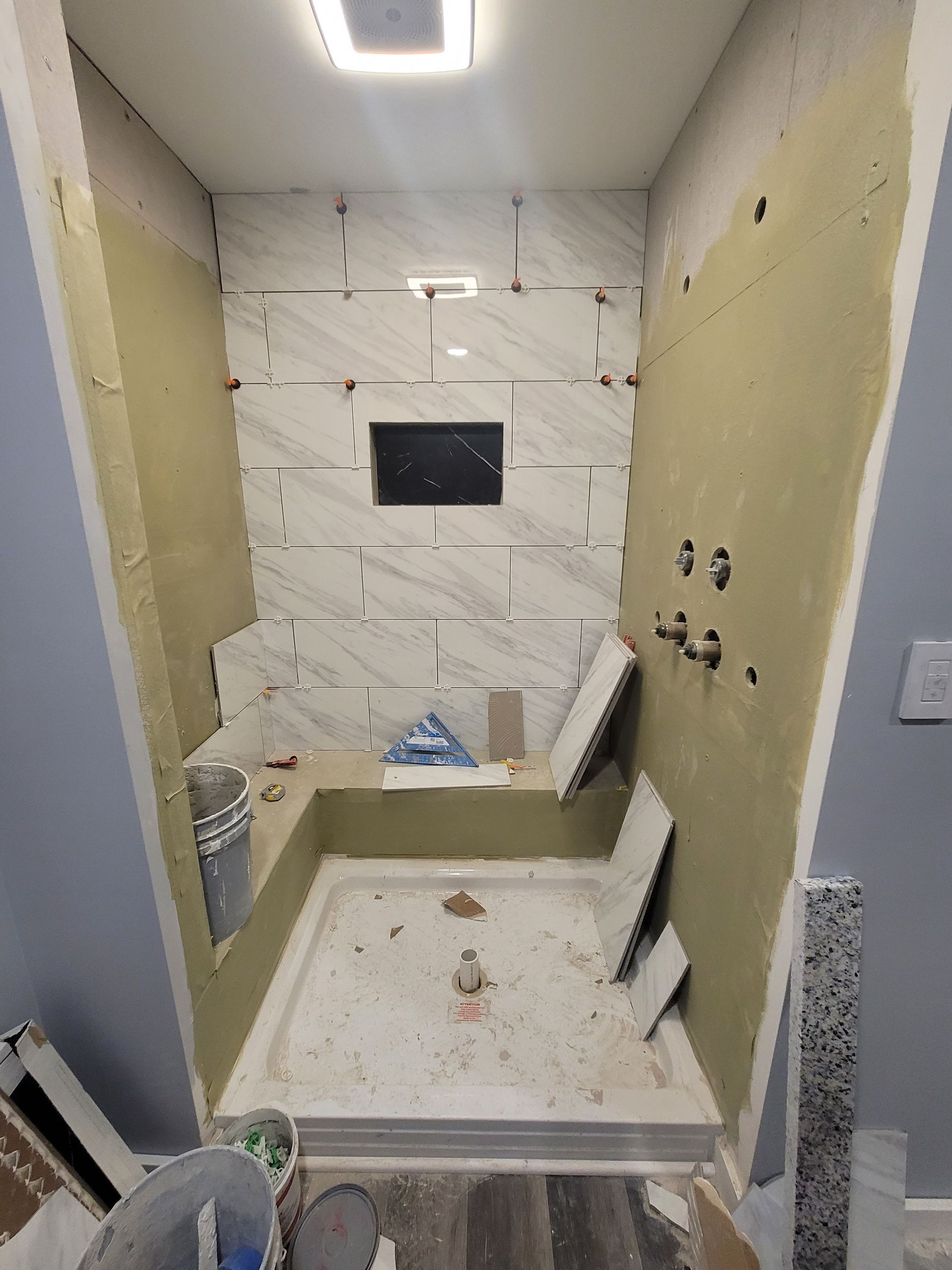 Bathroom under construction with tiled walls, a built-in bench, and shower fixtures.