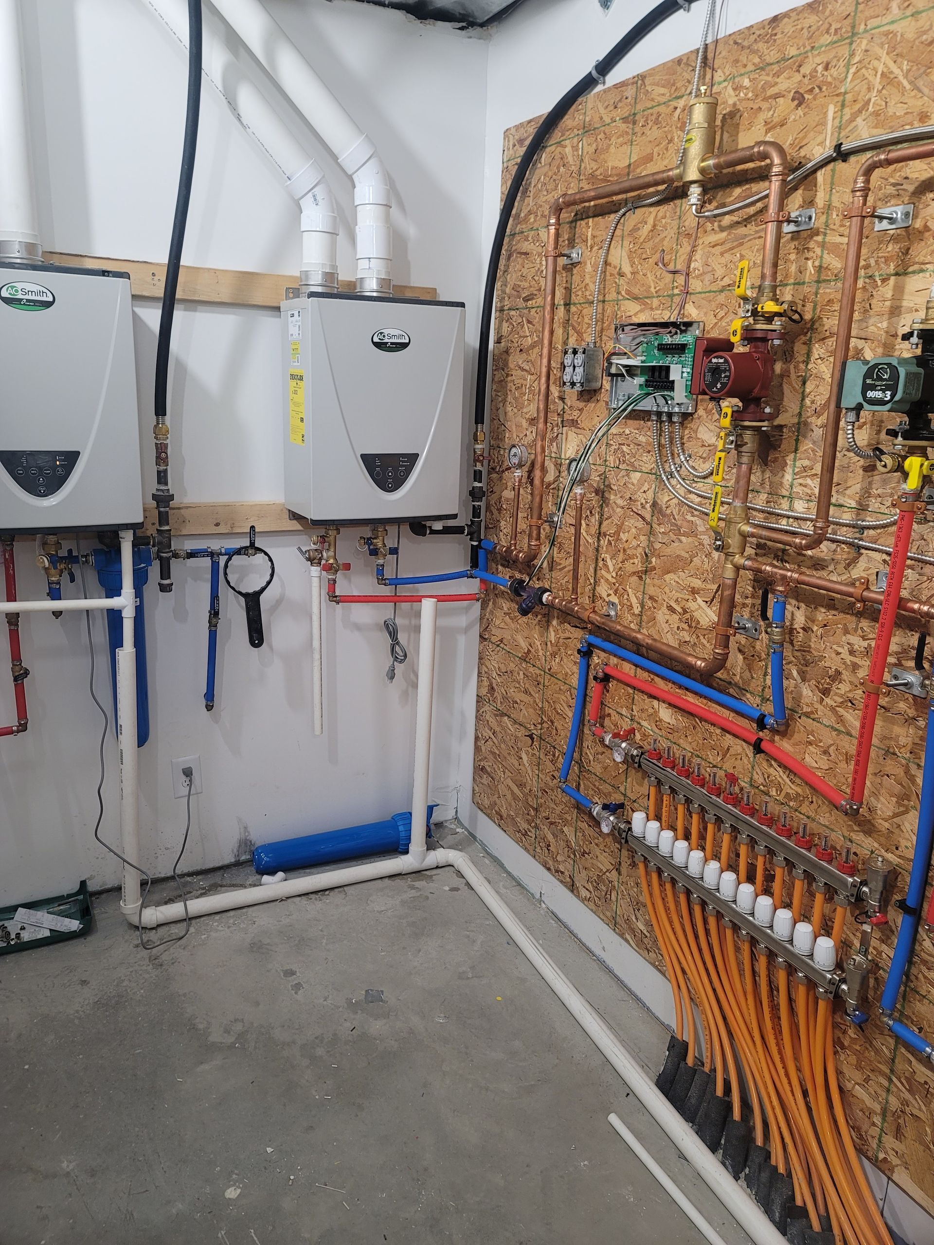 Water heater and radiant floor heating system with copper and PEX pipes on a wall.