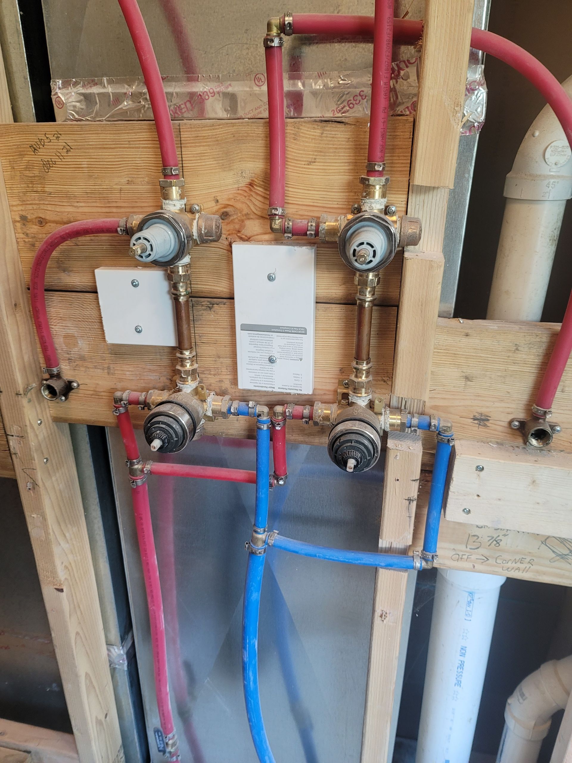 Piping system with red and blue PEX tubing and chrome fixtures installed on wooden studs.