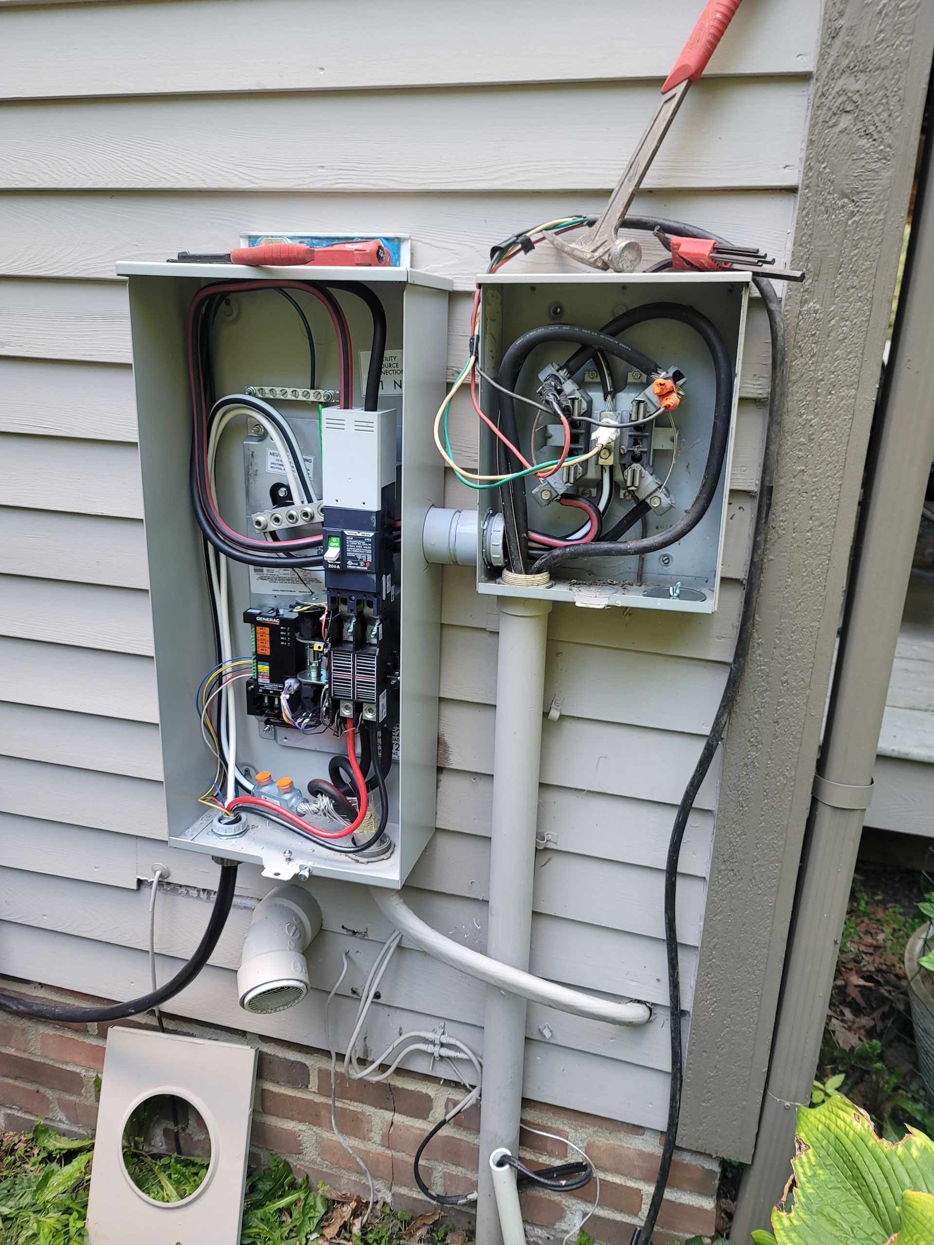 Open electrical boxes mounted on a house exterior, showing wiring and components.