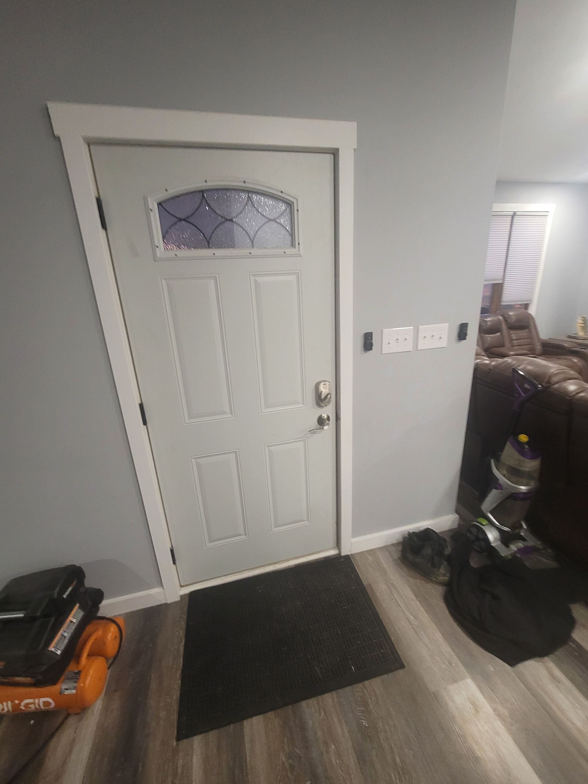 A light-gray front door with glass panel and black mat; the door is framed by white trim, set in a light-blue-gray room.