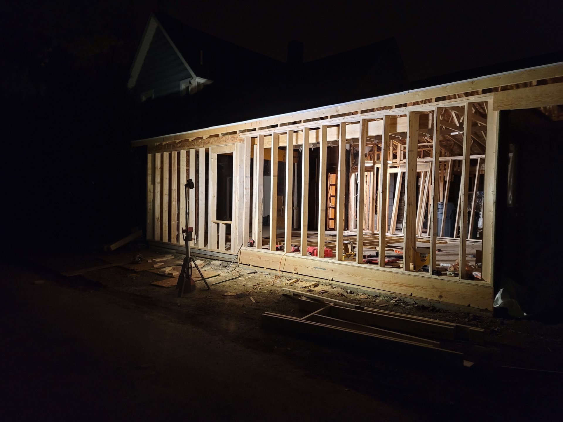 Night shot of a wooden house frame under construction, lit by a spotlight; dark background.