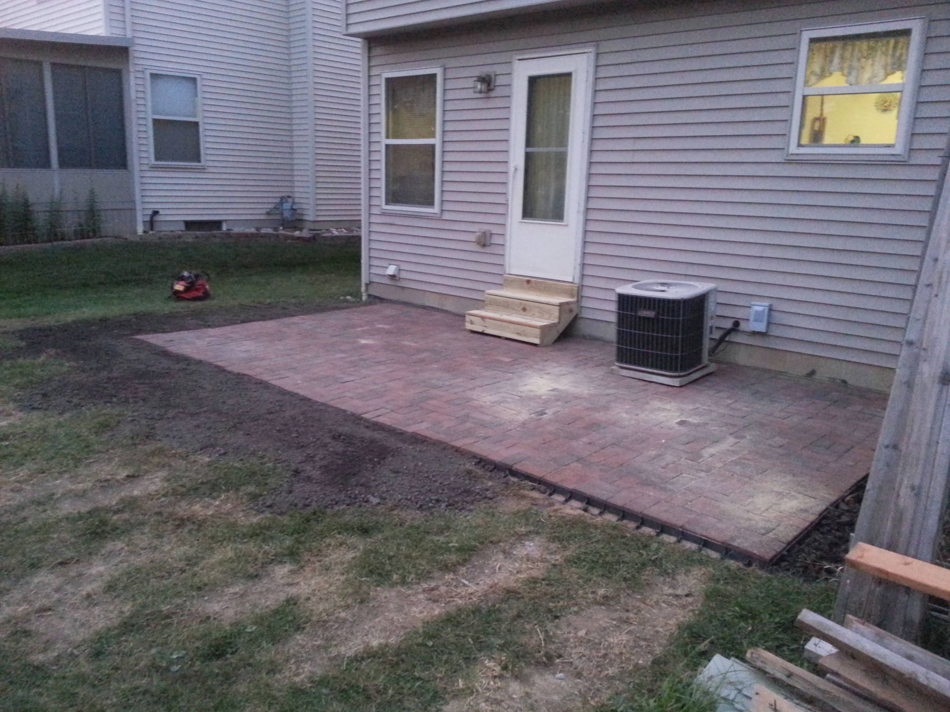 A new brick patio outside a house. A/C unit sits on the patio. Steps lead to the back door.