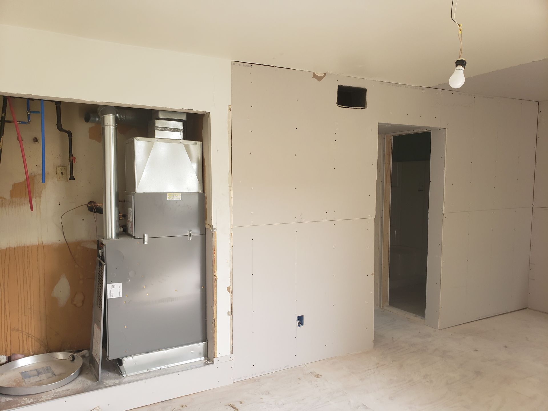 Interior view of a room under construction, with HVAC unit visible, drywall, and doorway.