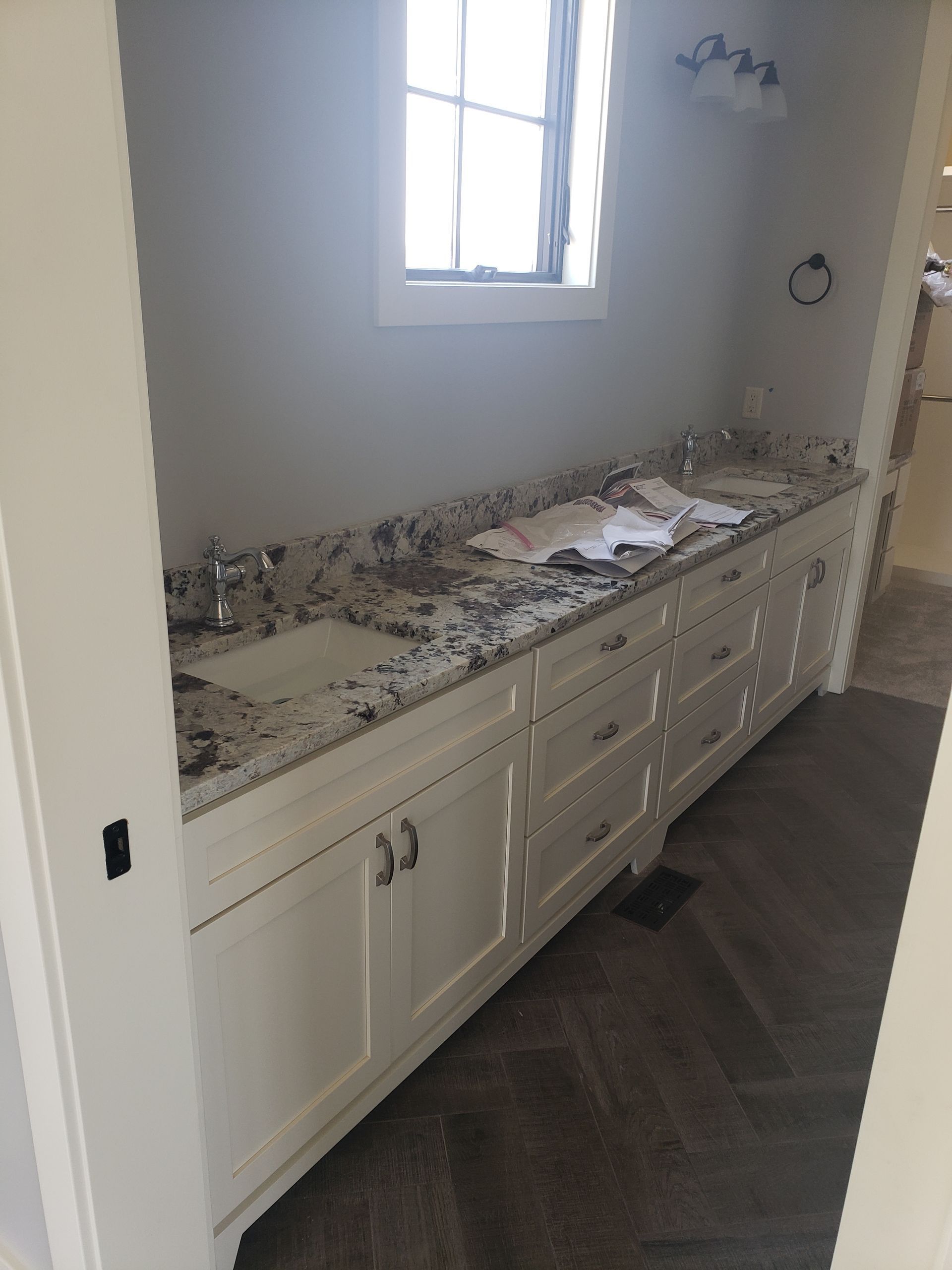 White vanity with granite countertop, two sinks, and window above.