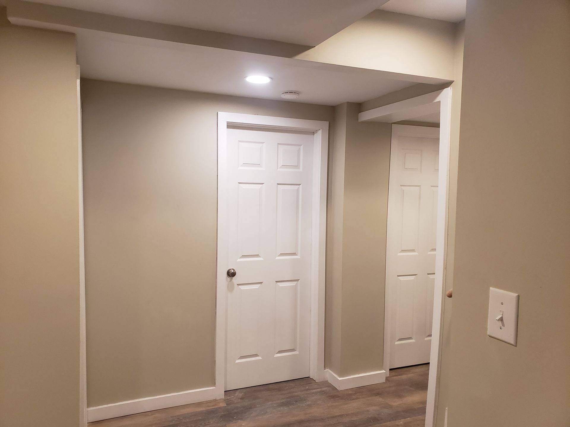 Hallway with two white doors, tan walls, and a light fixture.