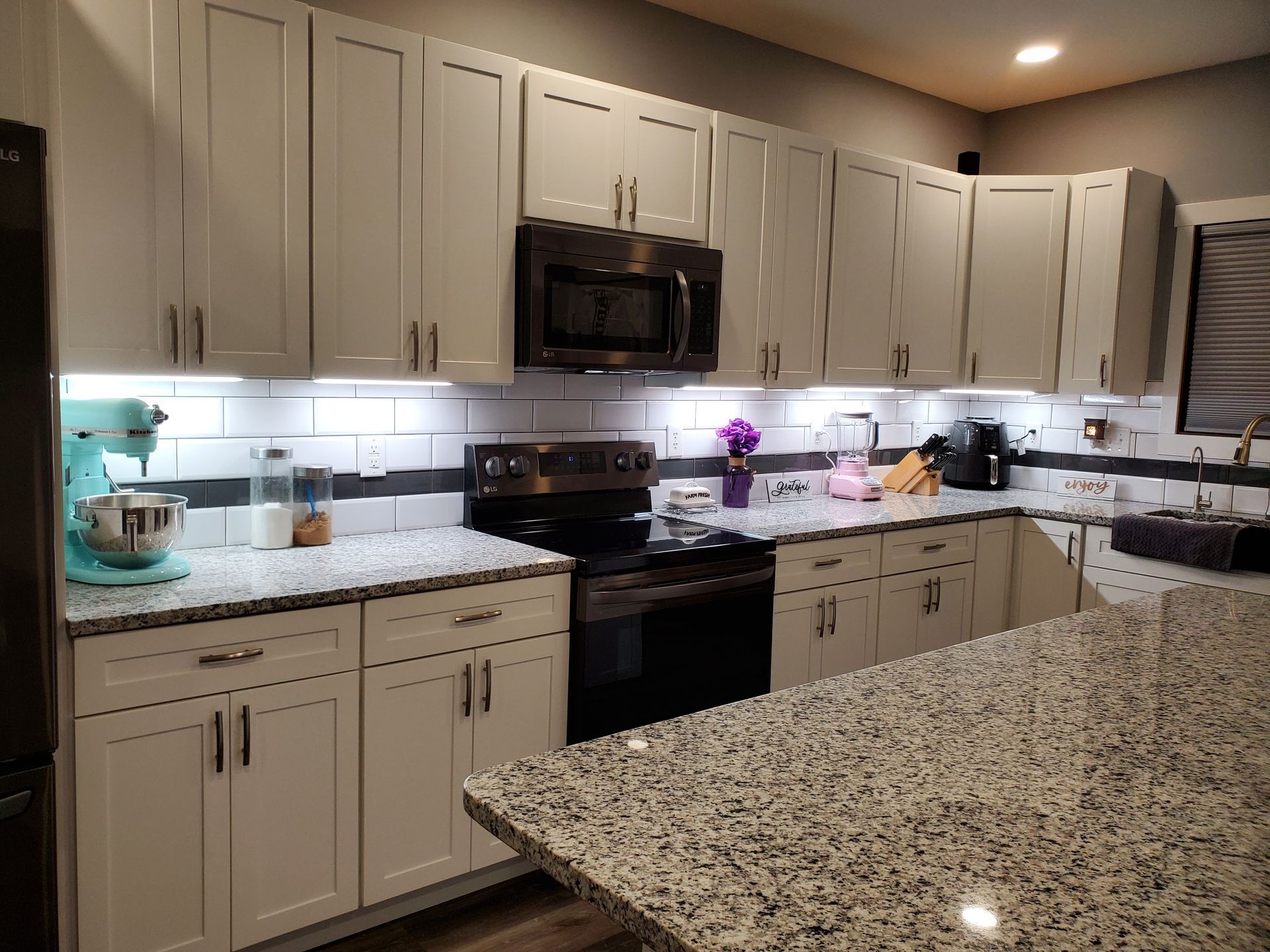 Modern kitchen with light gray cabinets, stainless steel appliances, and granite countertops.
