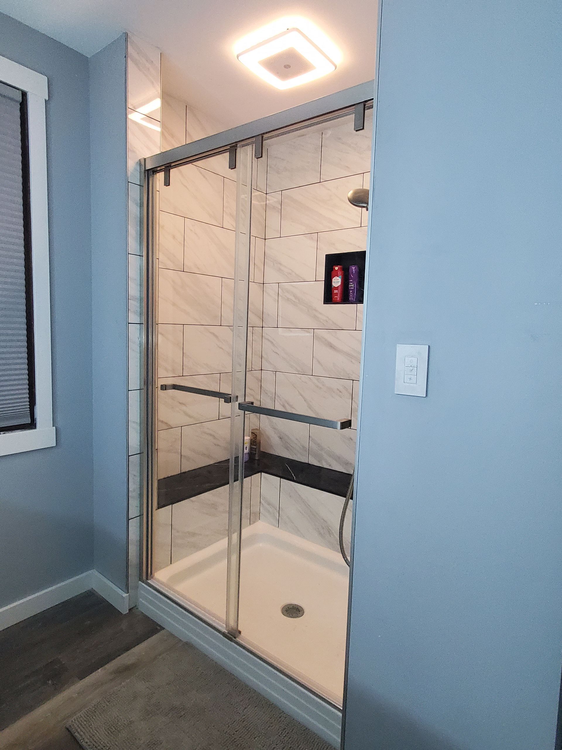 A modern bathroom with a glass shower, white and gray tiles, and blue walls.