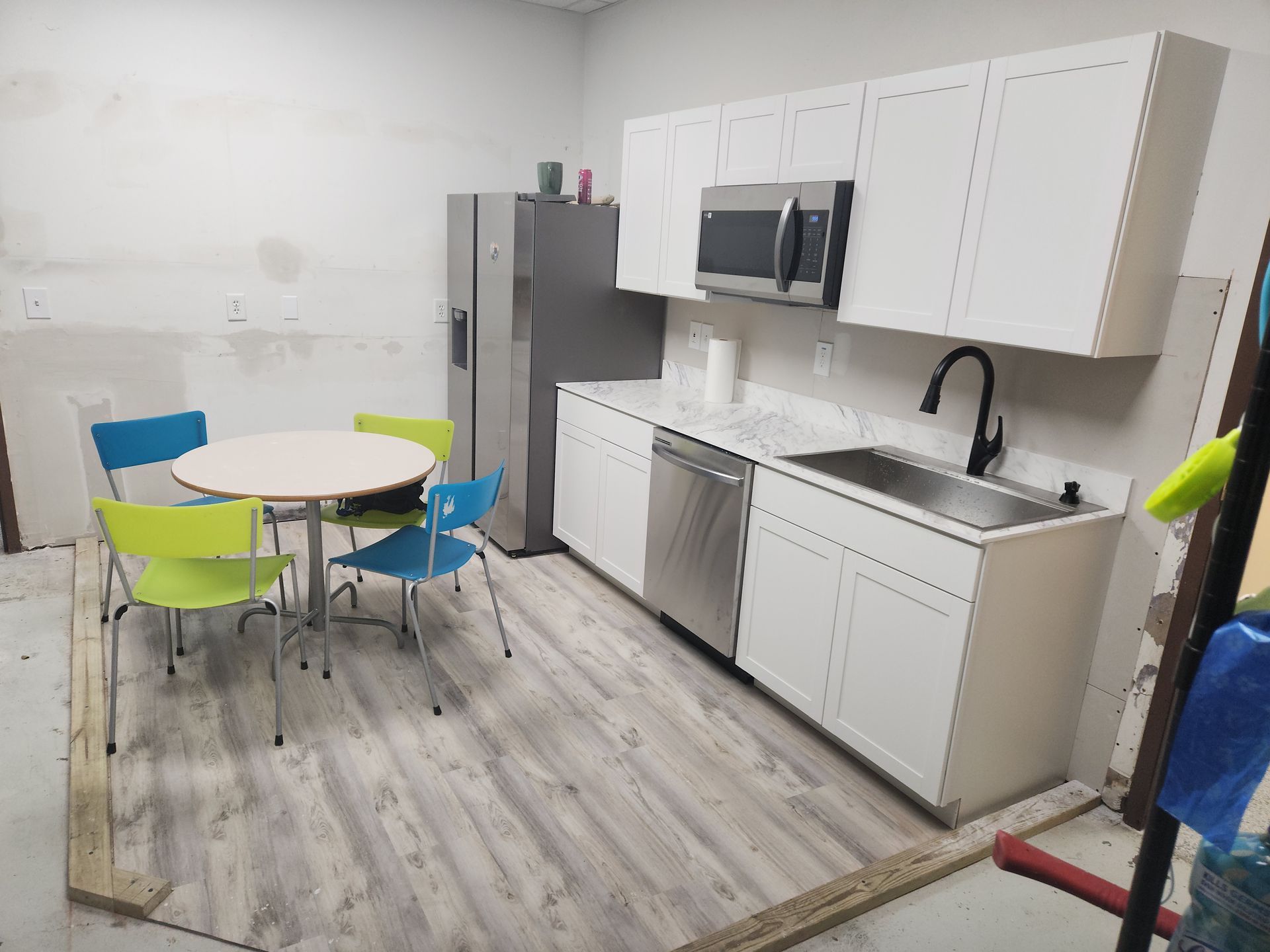 A small kitchen area with white cabinets, a stainless steel fridge and appliances, and a round table with colorful chairs.
