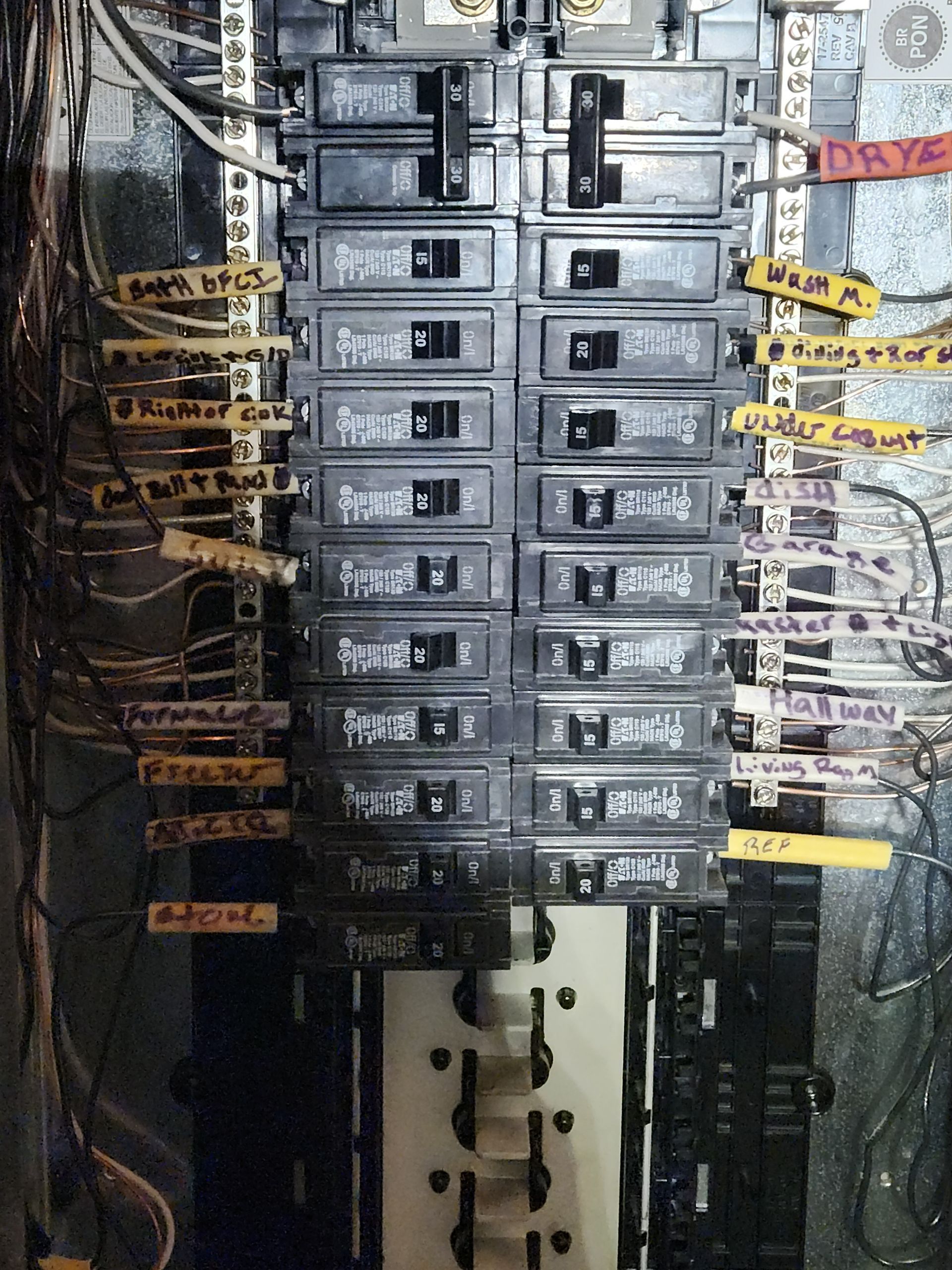 Electrical panel with circuit breakers and handwritten labels. Wires are visible on either side.