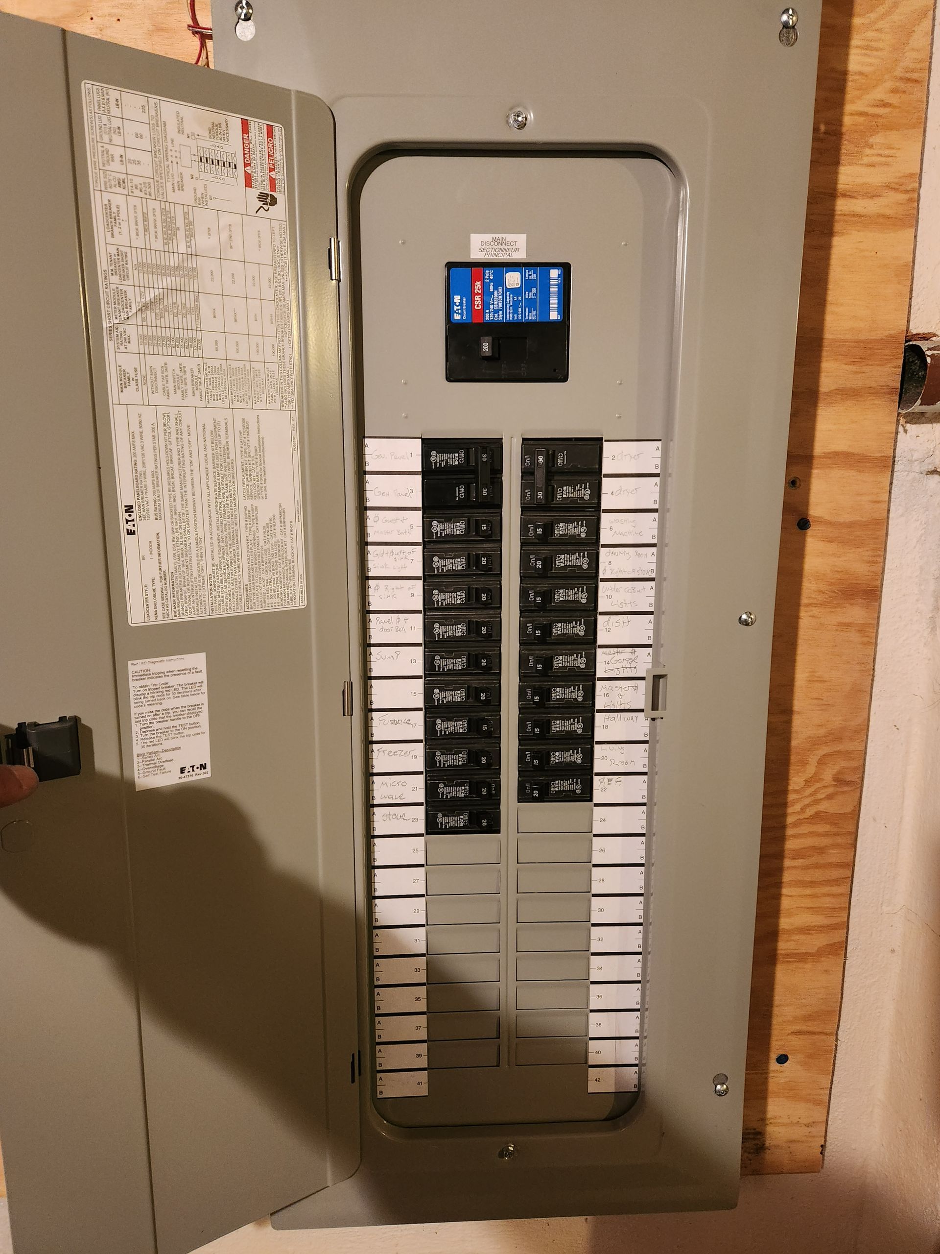Open gray electrical panel with circuit breakers, installed in a wooden wall.
