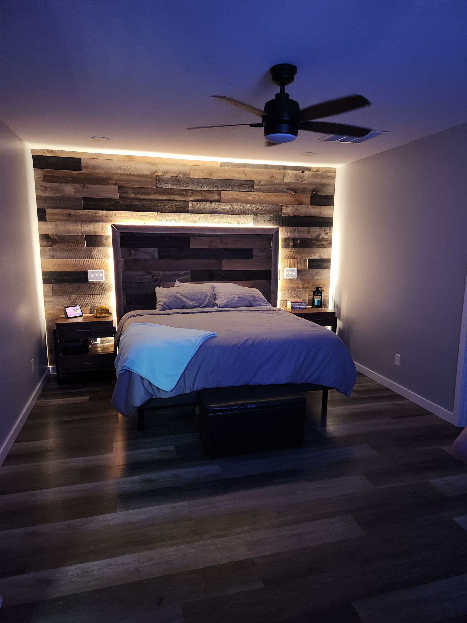 Bedroom with wood accent wall, bed, nightstands, and blue ambient lighting.