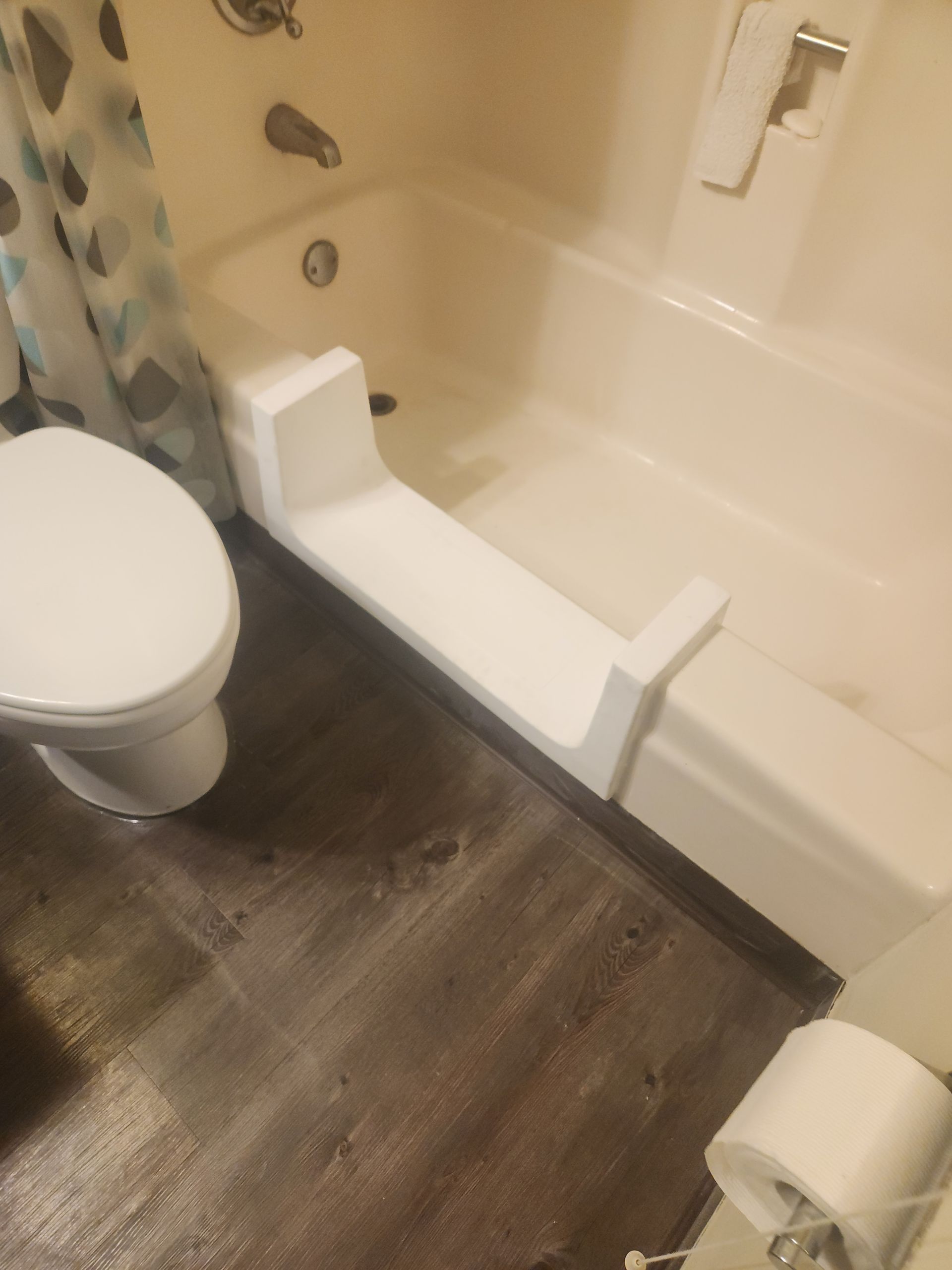 Bathroom with a walk-in bathtub, toilet, and shower curtain; dark wood-look floor and white fixtures.