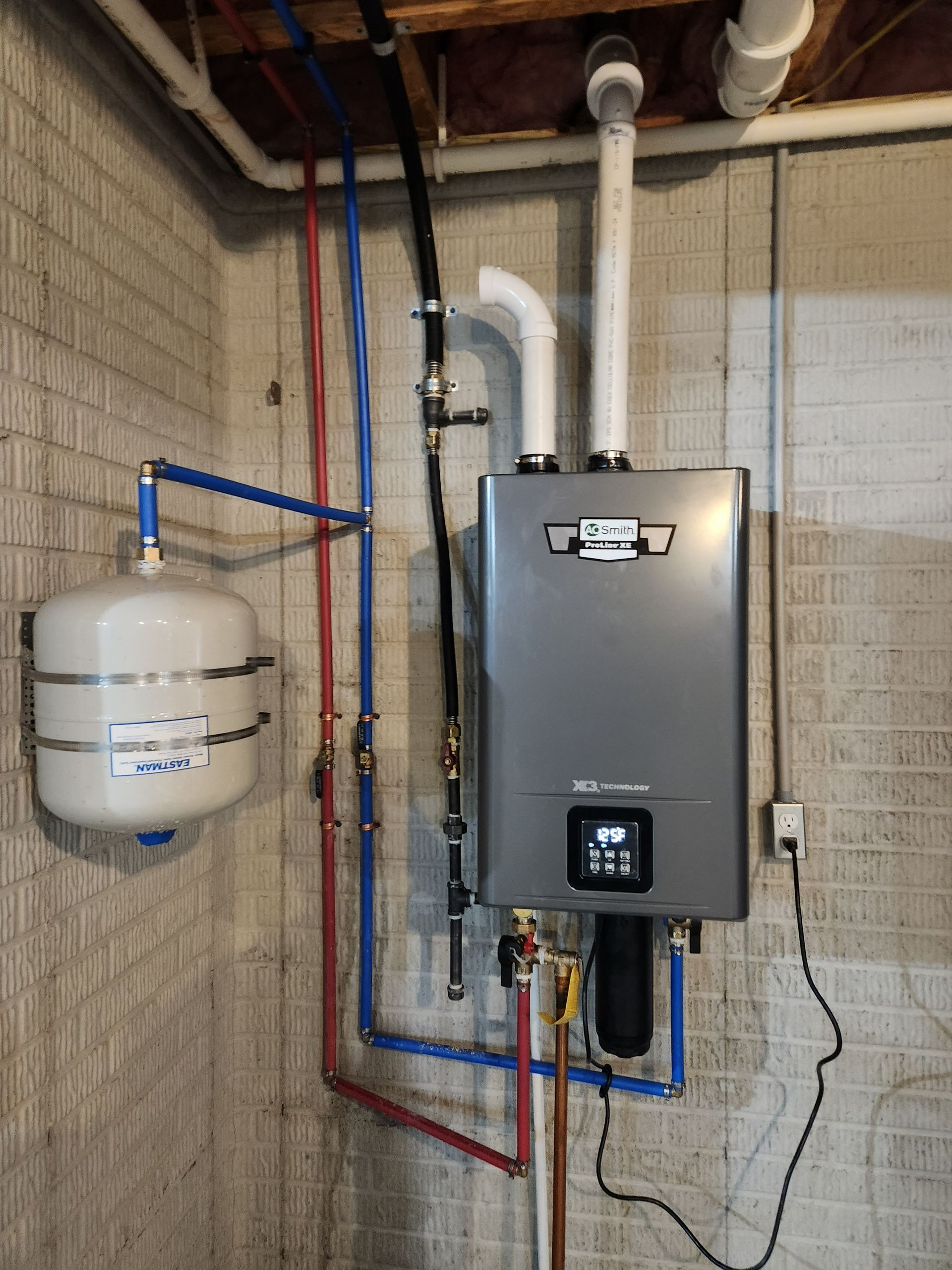 Tankless water heater installed on a concrete wall, with blue and red pipes and a white expansion tank.