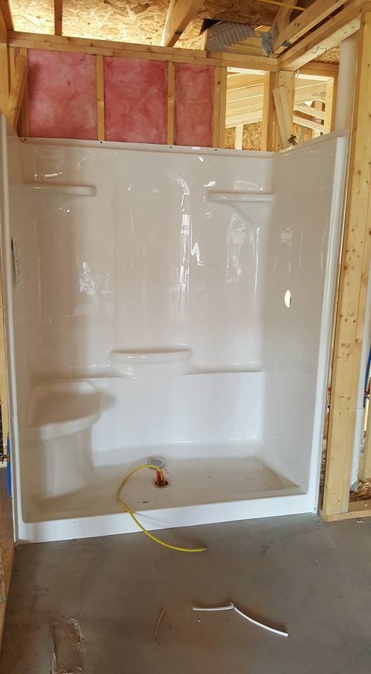 White shower stall installed in a wood-framed bathroom under construction; pink insulation visible.