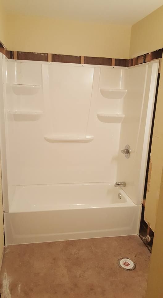 White shower/tub combo unit in a bathroom undergoing renovation; brown framing and tan wall.