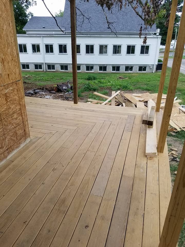 Wooden deck with stairs under construction, leading toward a white building.