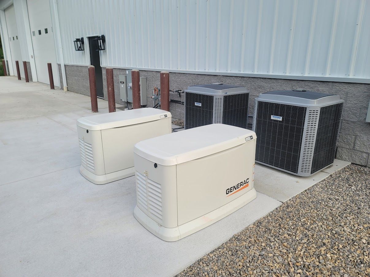 Two beige generators and two black air conditioners sit on a concrete pad next to a white building.
