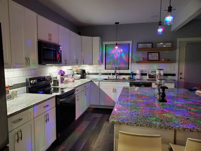 Kitchen with white cabinets, granite countertops, stainless steel appliances, and colorful lights.