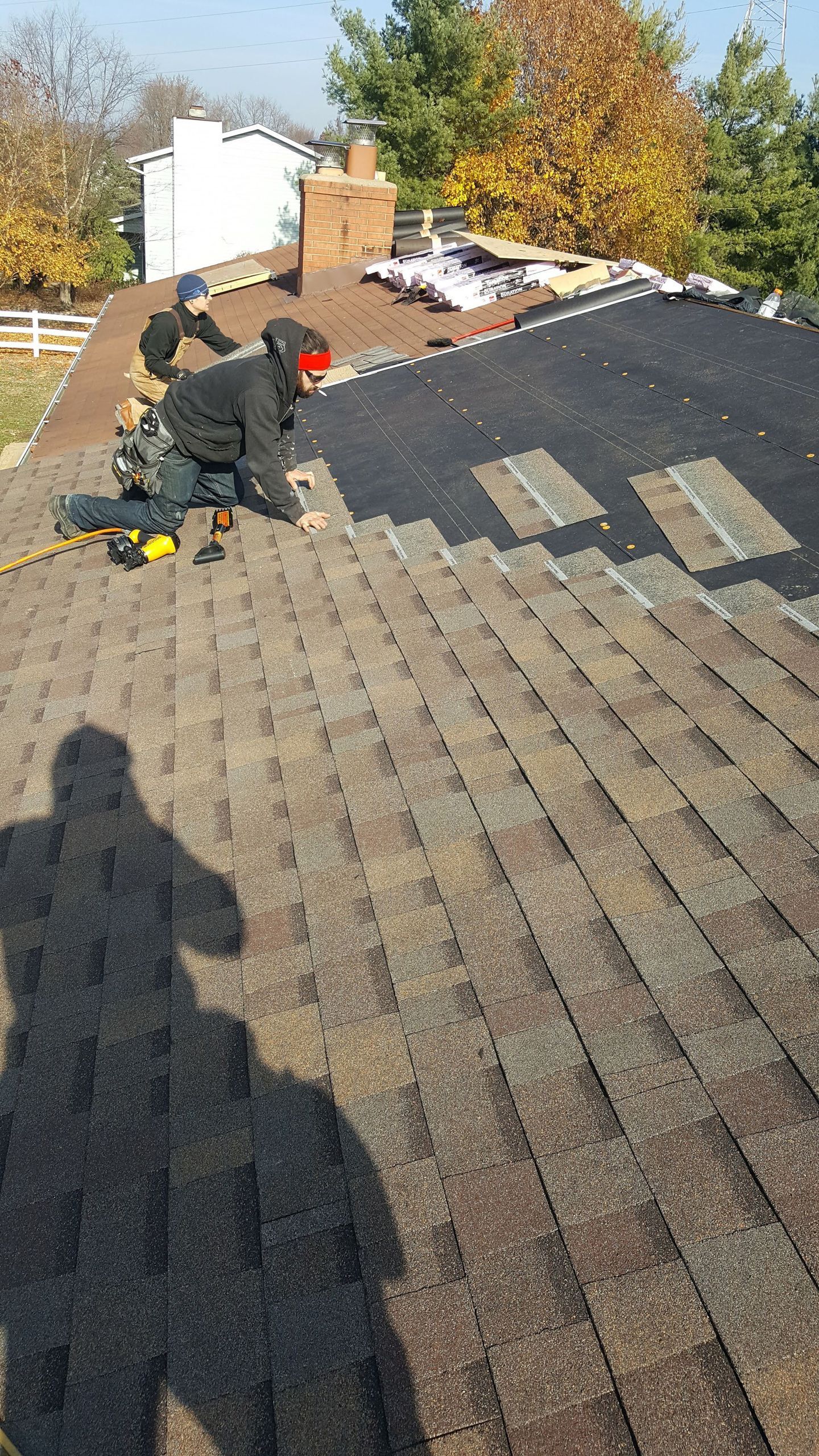Two roofers on a brown shingle roof, replacing shingles. Sunny day.