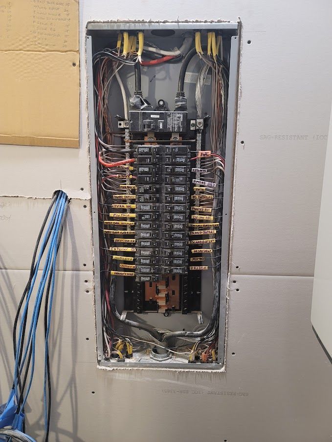 Electrical panel with numerous circuit breakers, wires, and busbars, installed in a wall.
