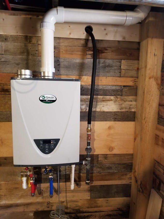 White tankless water heater mounted on a wood-paneled wall, with pipes and vents visible.