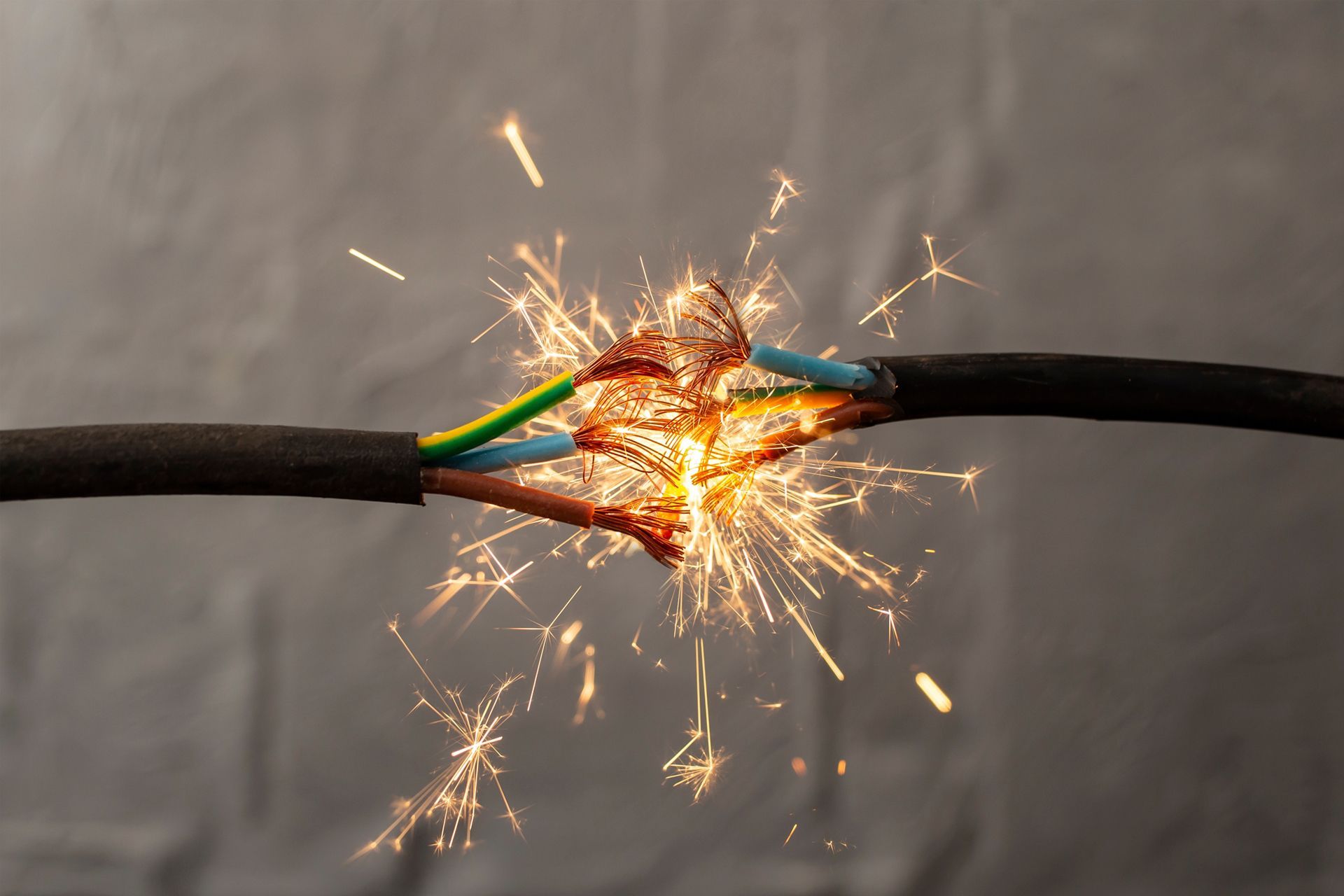 Hands using wire stripper to remove insulation from a green wire inside a wall box with colorful wires.
