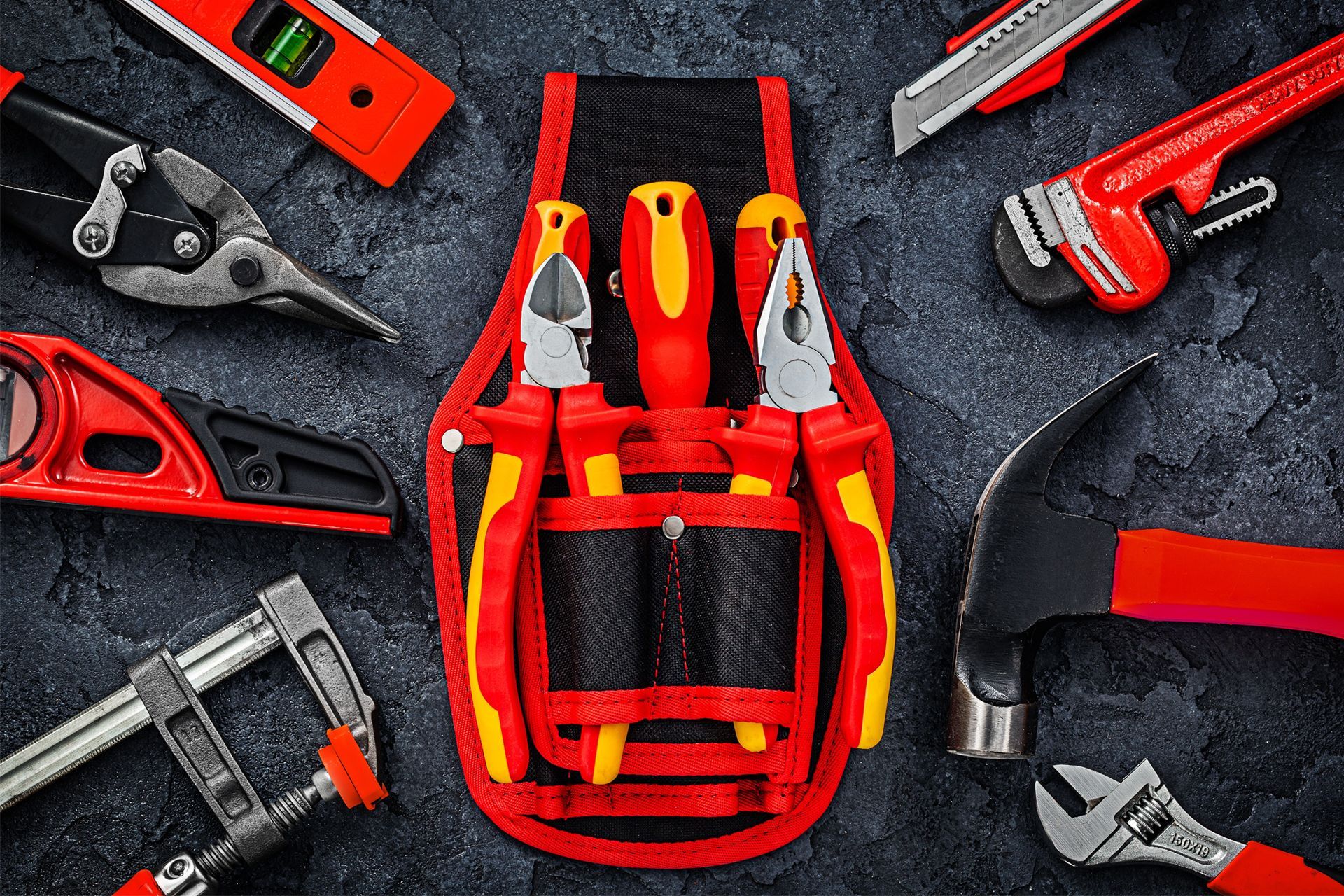 Red and yellow tools arranged around a central tool belt on a dark textured surface.