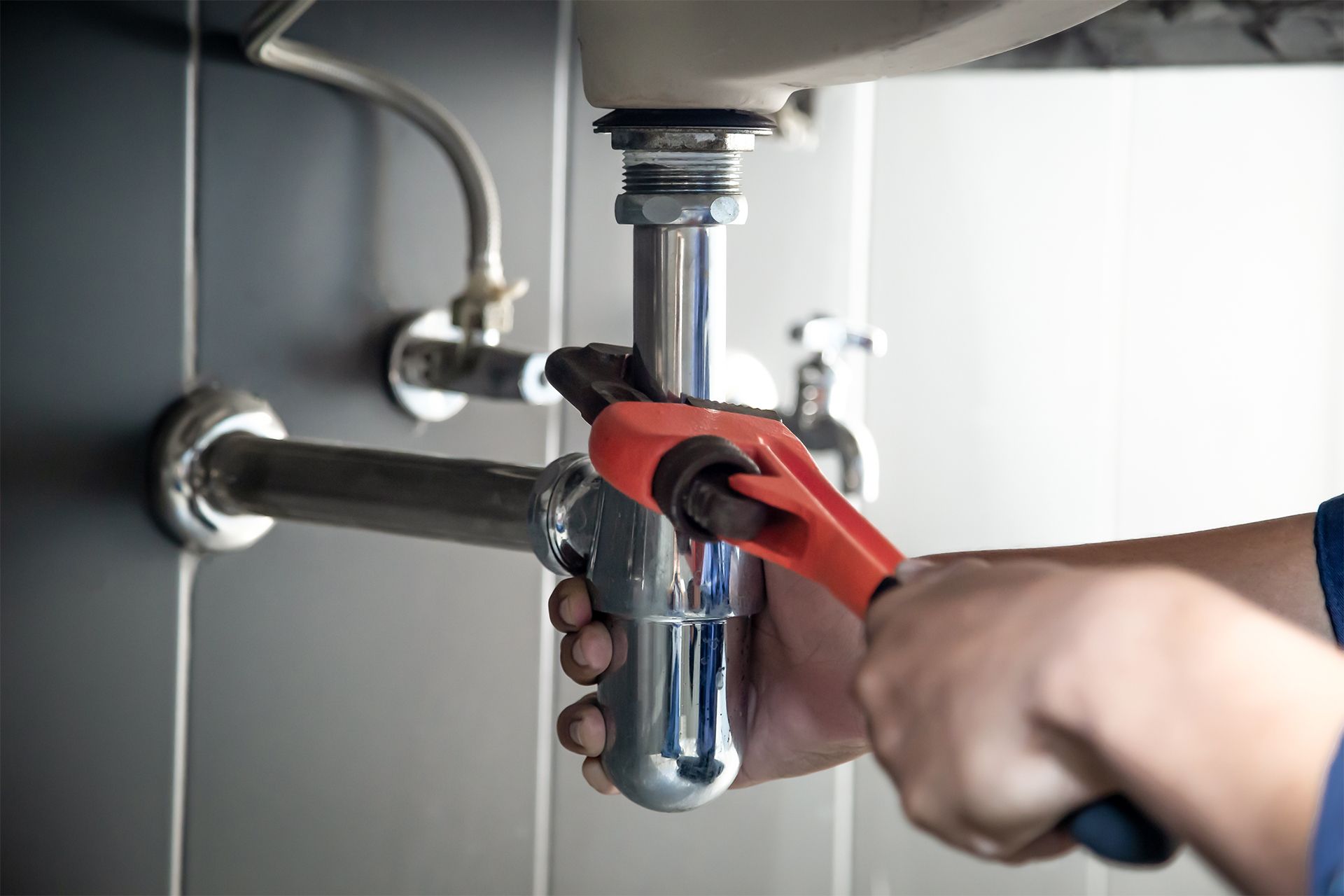Plumber using a wrench to repair pipes under a sink.