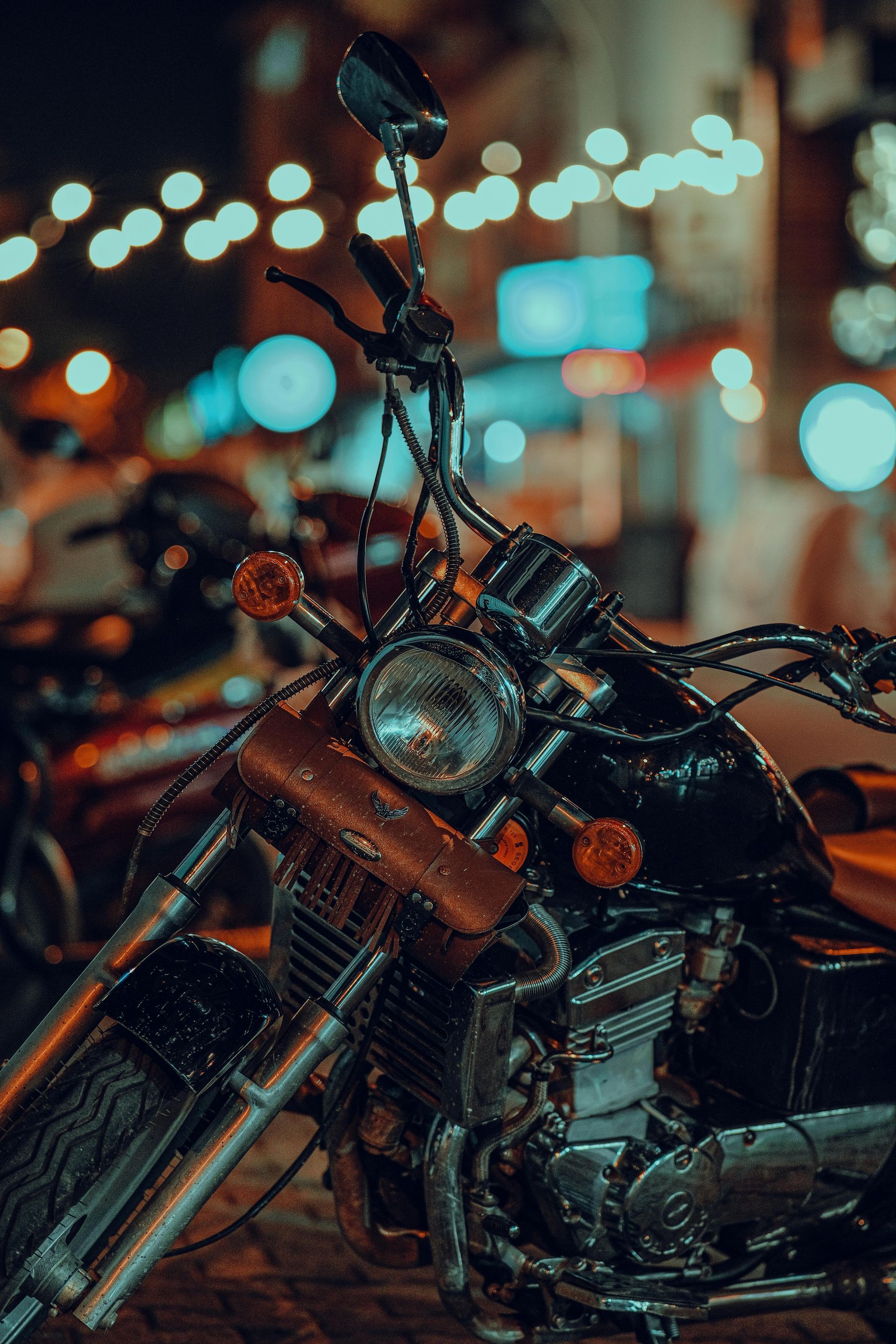 A black motorcycle parked on a brick street at night, with blurred city lights in the background.