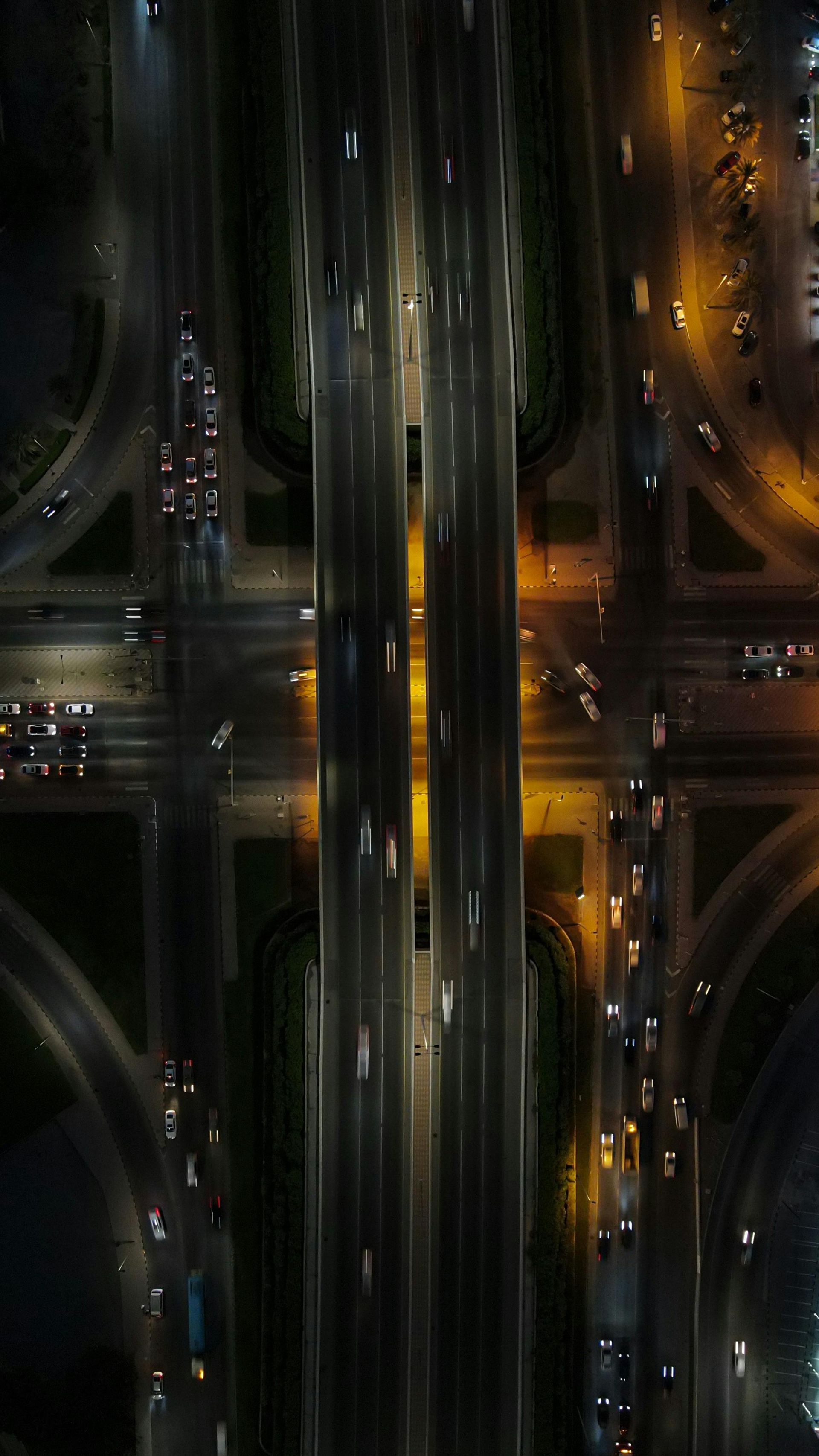 An aerial night view of a multi-level highway interchange with bright streaks of light from moving traffic.