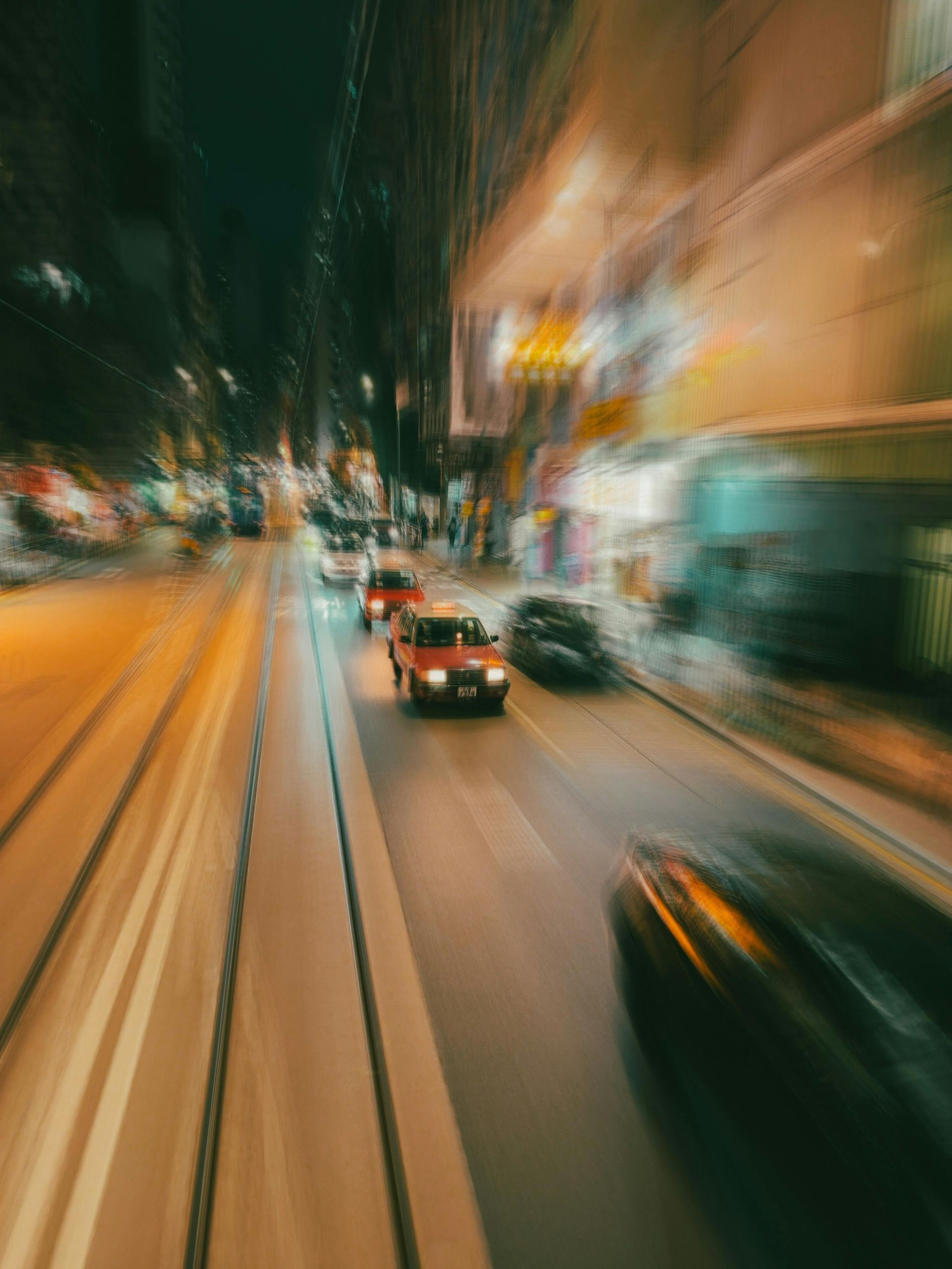 A high-speed motion blur shot of a city street at night, with car headlights and traffic moving along tram tracks.