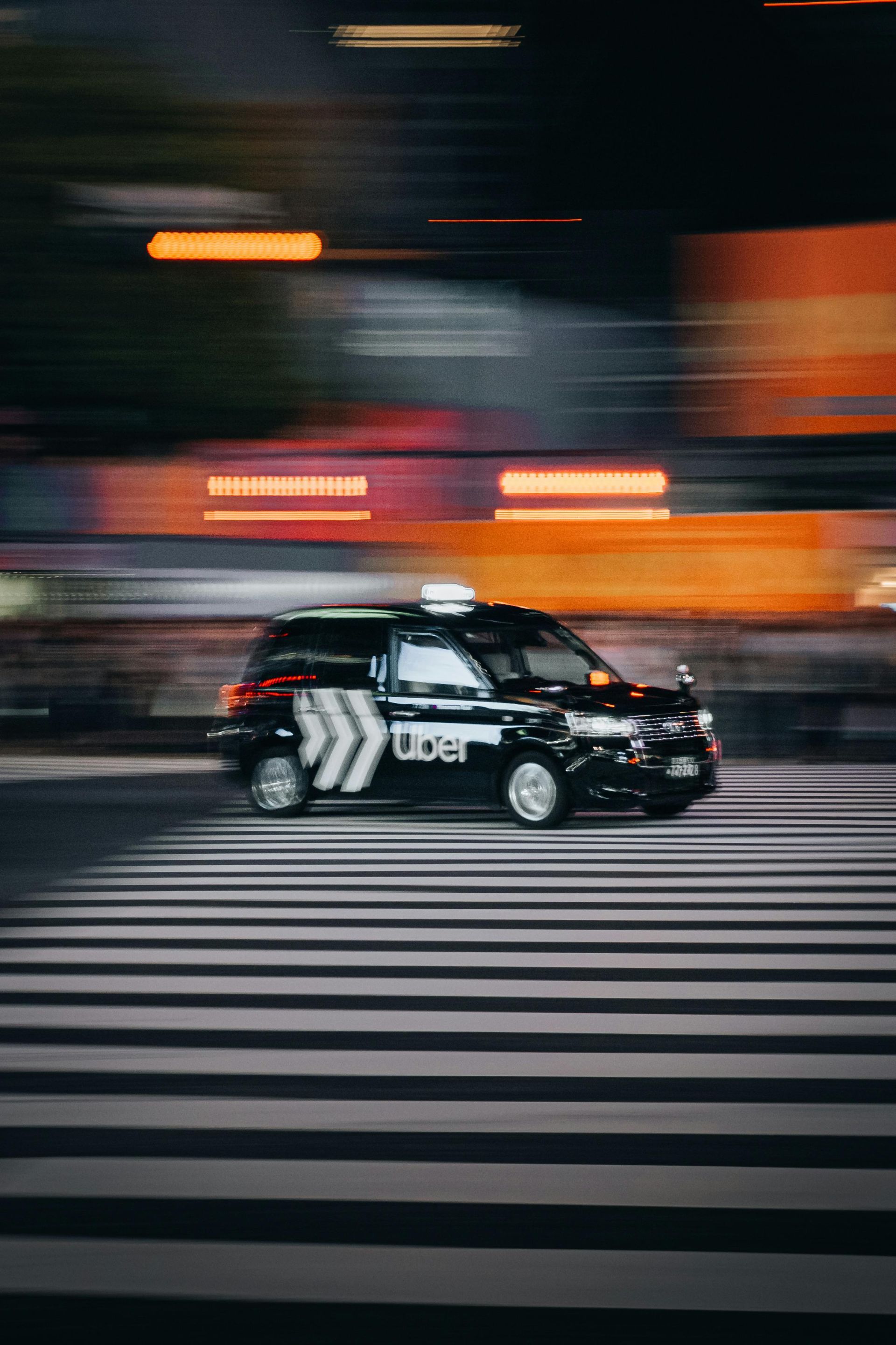 A black Uber taxi driving across a crosswalk at night, with motion blur in the background.