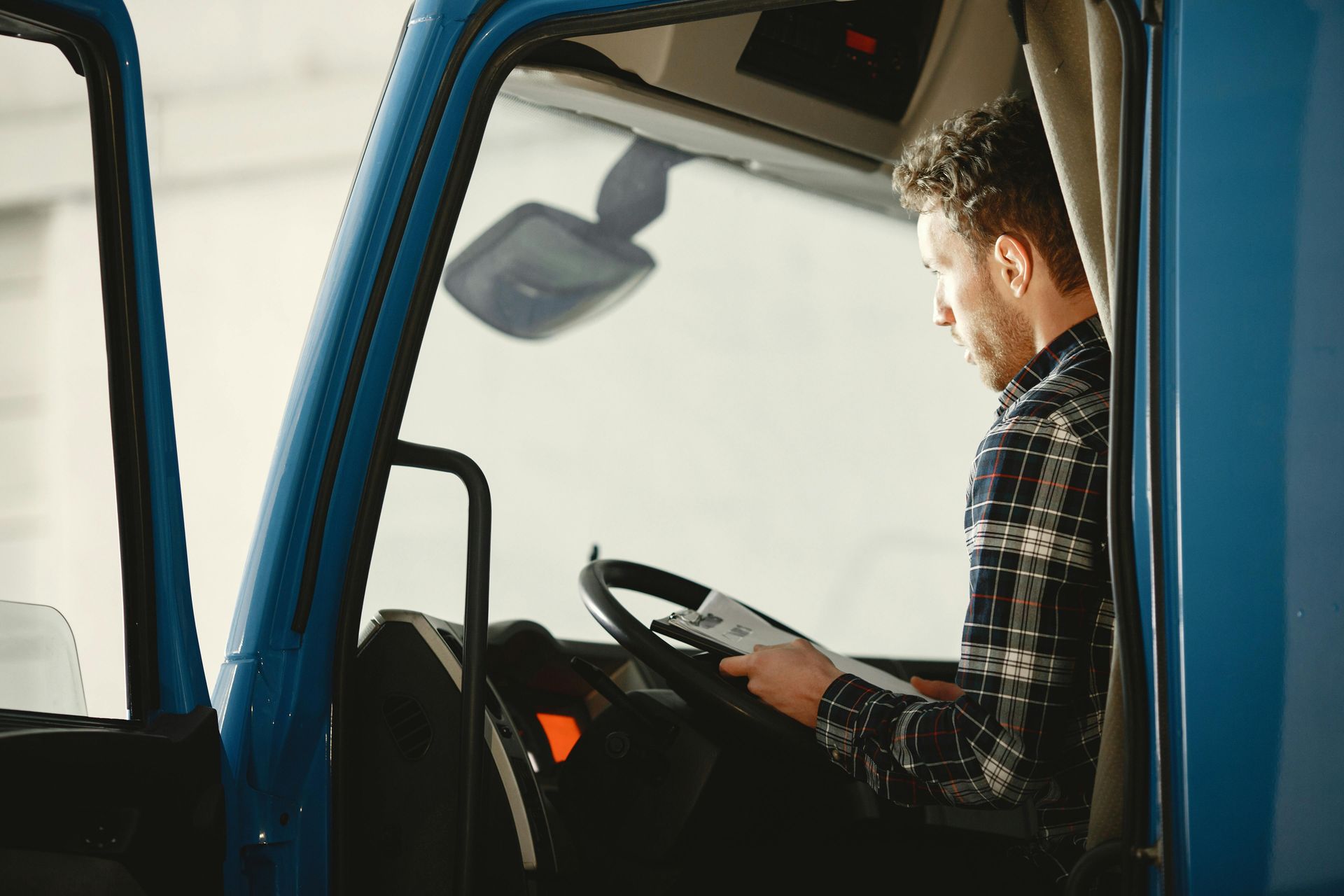 A person in a plaid shirt sits in the driver's seat of a blue truck, looking down at a document.