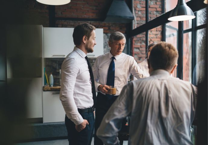 Two people in a kitchen, standing and sitting at a wooden table, smiling while looking at a document together.