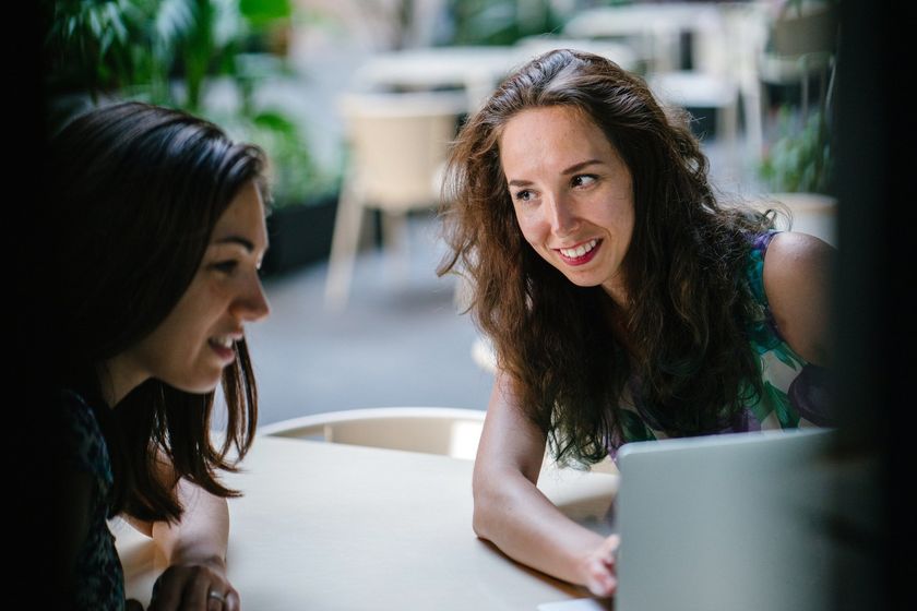 Dos mujeres están sentadas en una mesa mirando una computadora portátil.