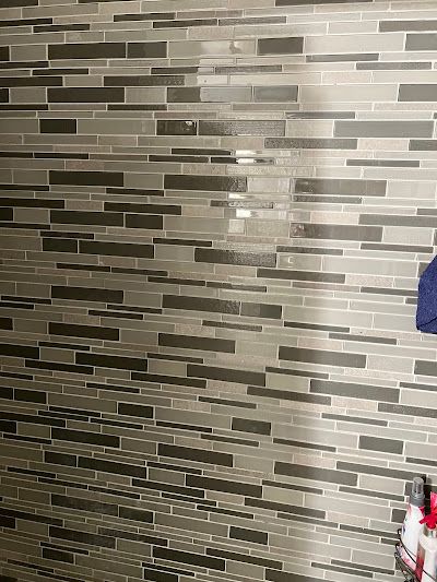 A person is standing in front of a tiled wall.