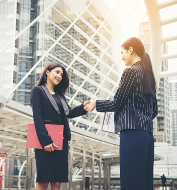 Two men in suits shaking hands in a warmly lit hotel lobby. They are smiling at each other.