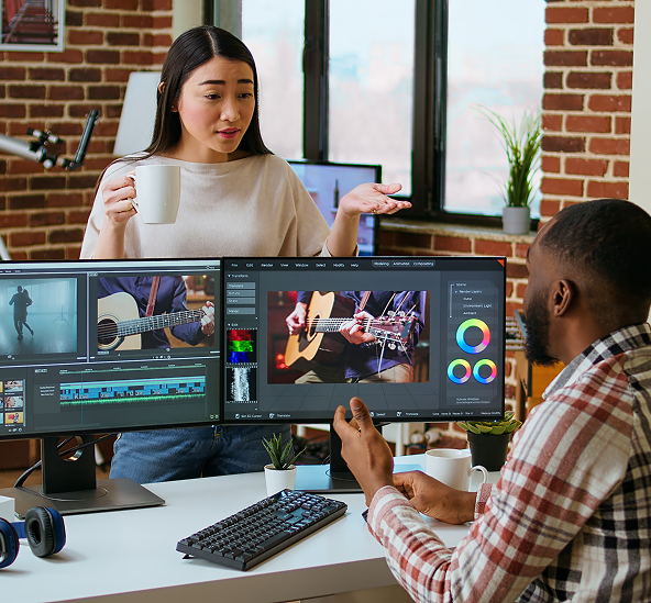 Woman in green sweater looks at computer screen with video editing software, holding a coffee mug; another woman edits.