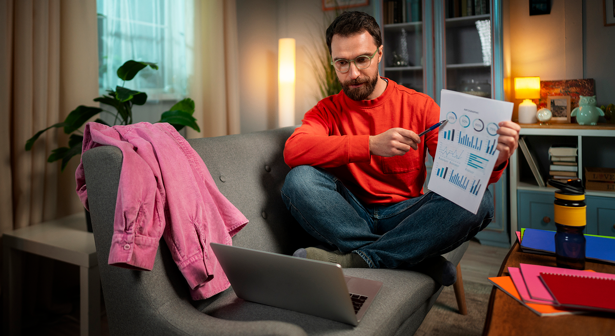 Man with beard in blue plaid shirt filming a video in a home studio. Camera and lamp in foreground.