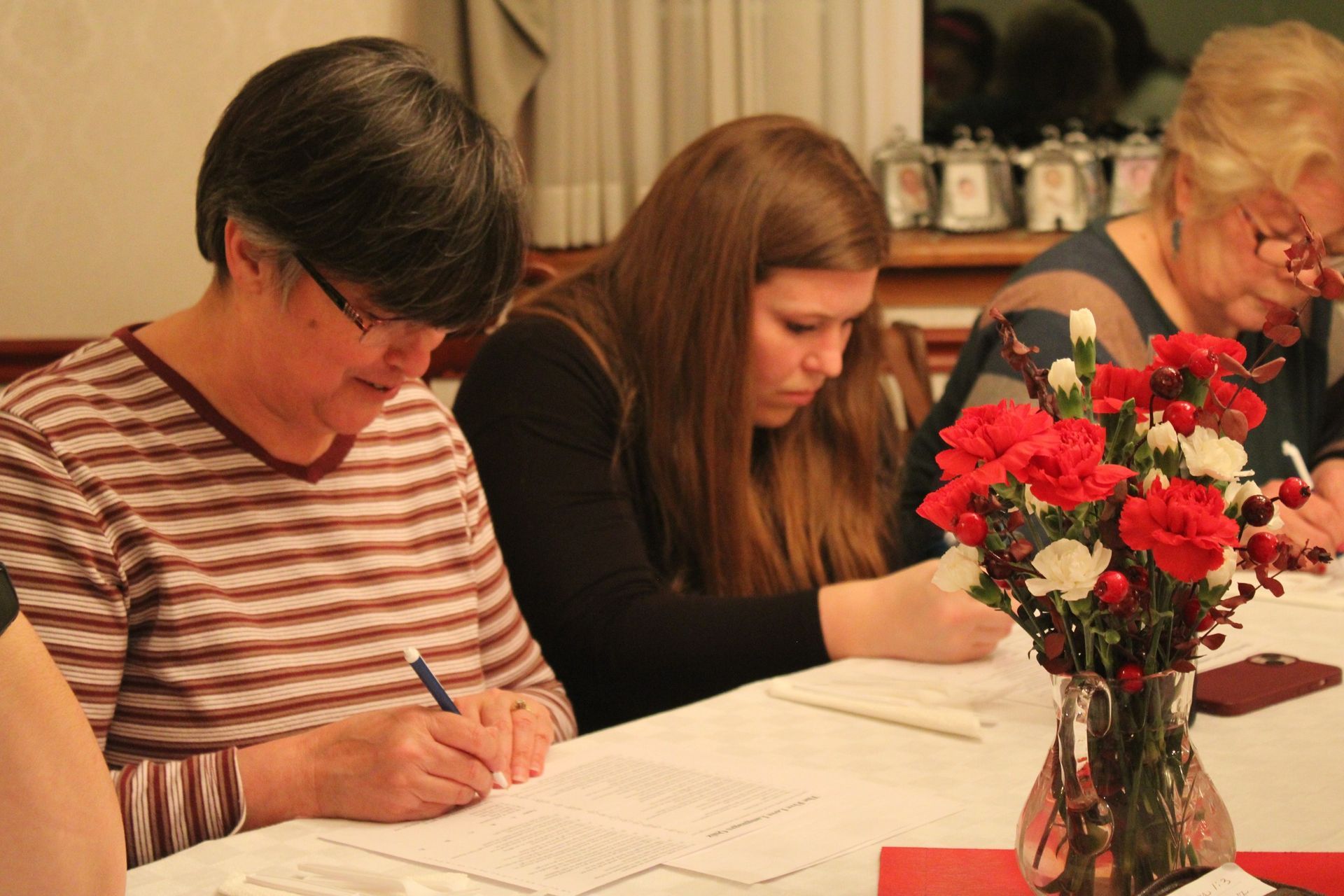 Three women are sitting at a table writing on a piece of paper