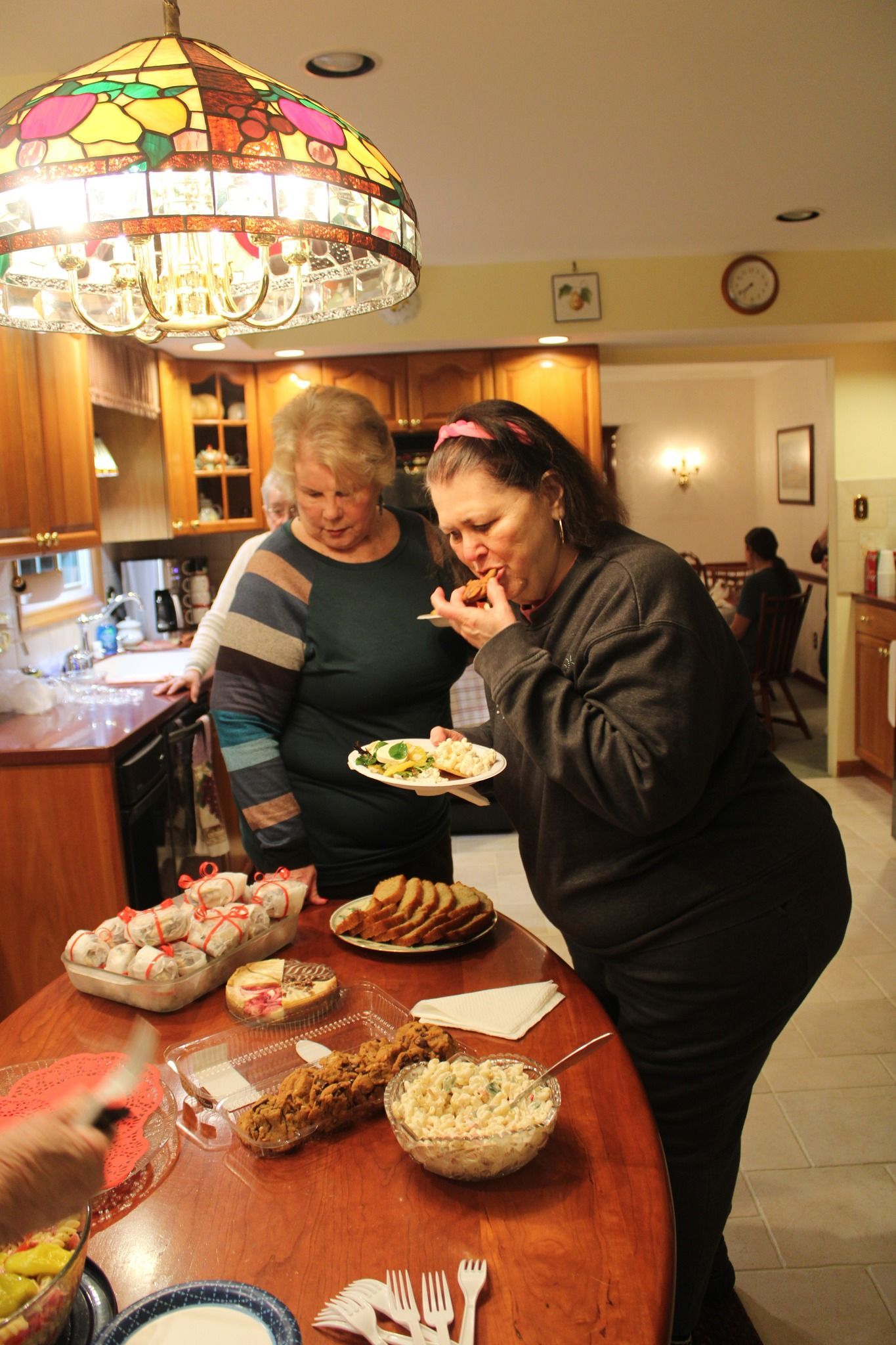 Two women are standing at a table with plates of food on it.