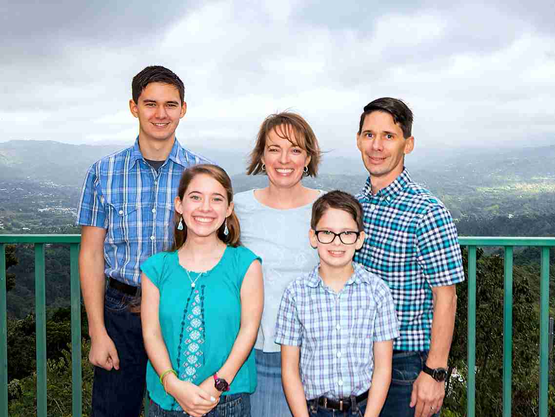 A family is posing for a picture on a balcony overlooking a mountain.