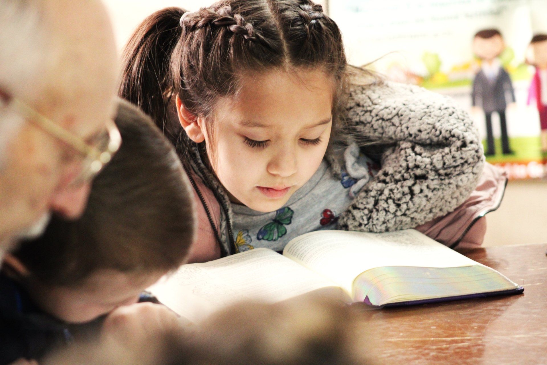 A little girl is sitting at a table reading a book.